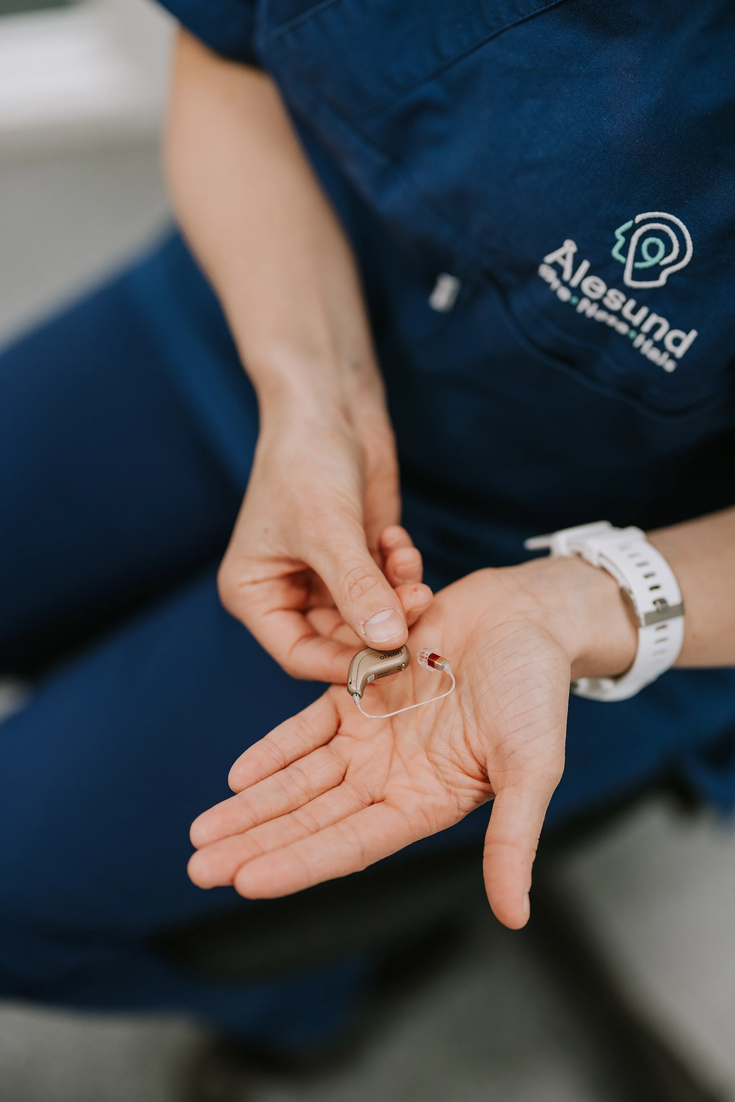 En person med en akustisk hørselsimplantat i hånden, iført en uniform med logoen Aarhus Universitetshospital.