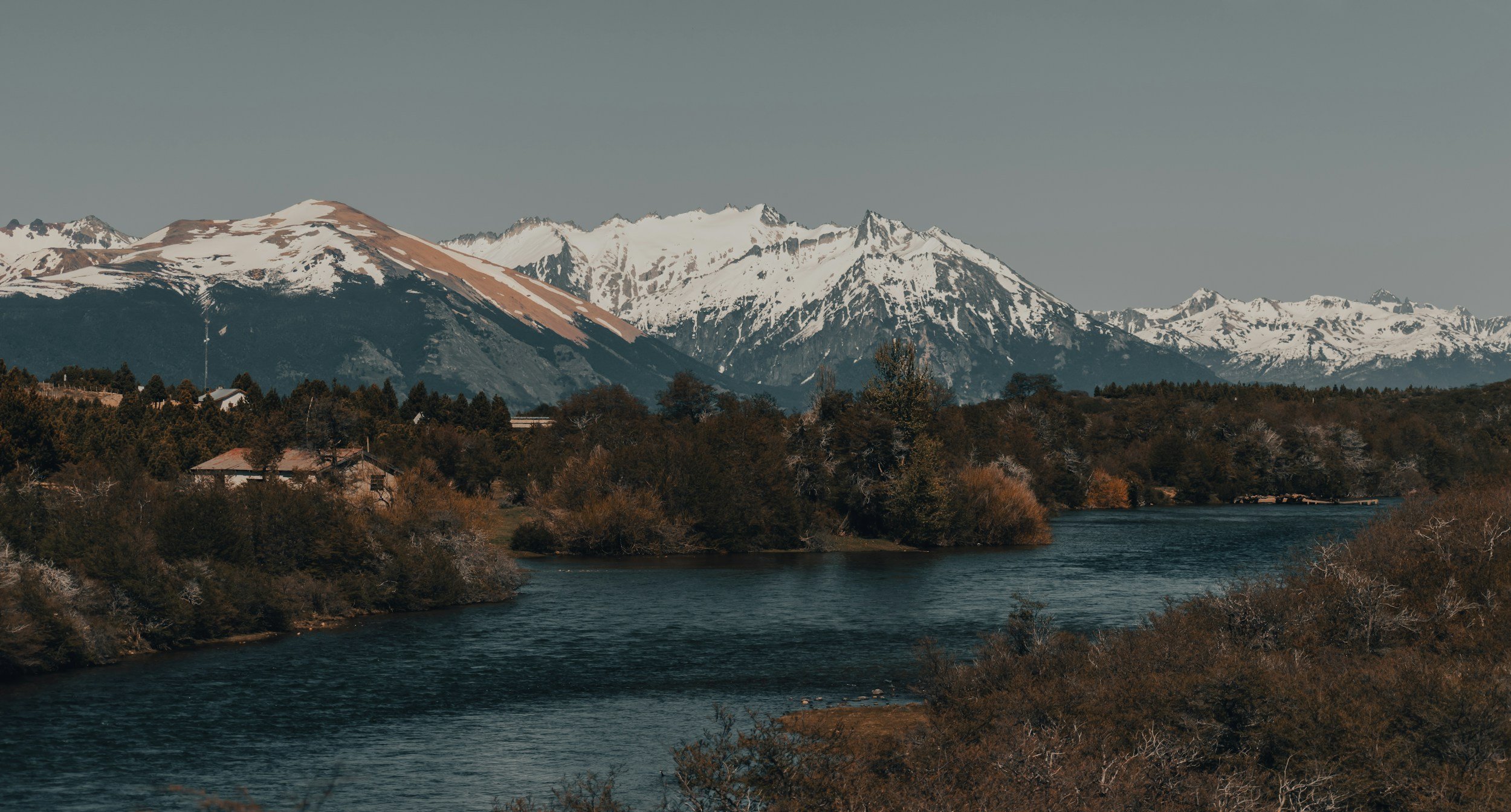 Scenic view of snow-capped mountains in Northern Nevada, a winding Truckee River, and lush trees in a natural landscape.