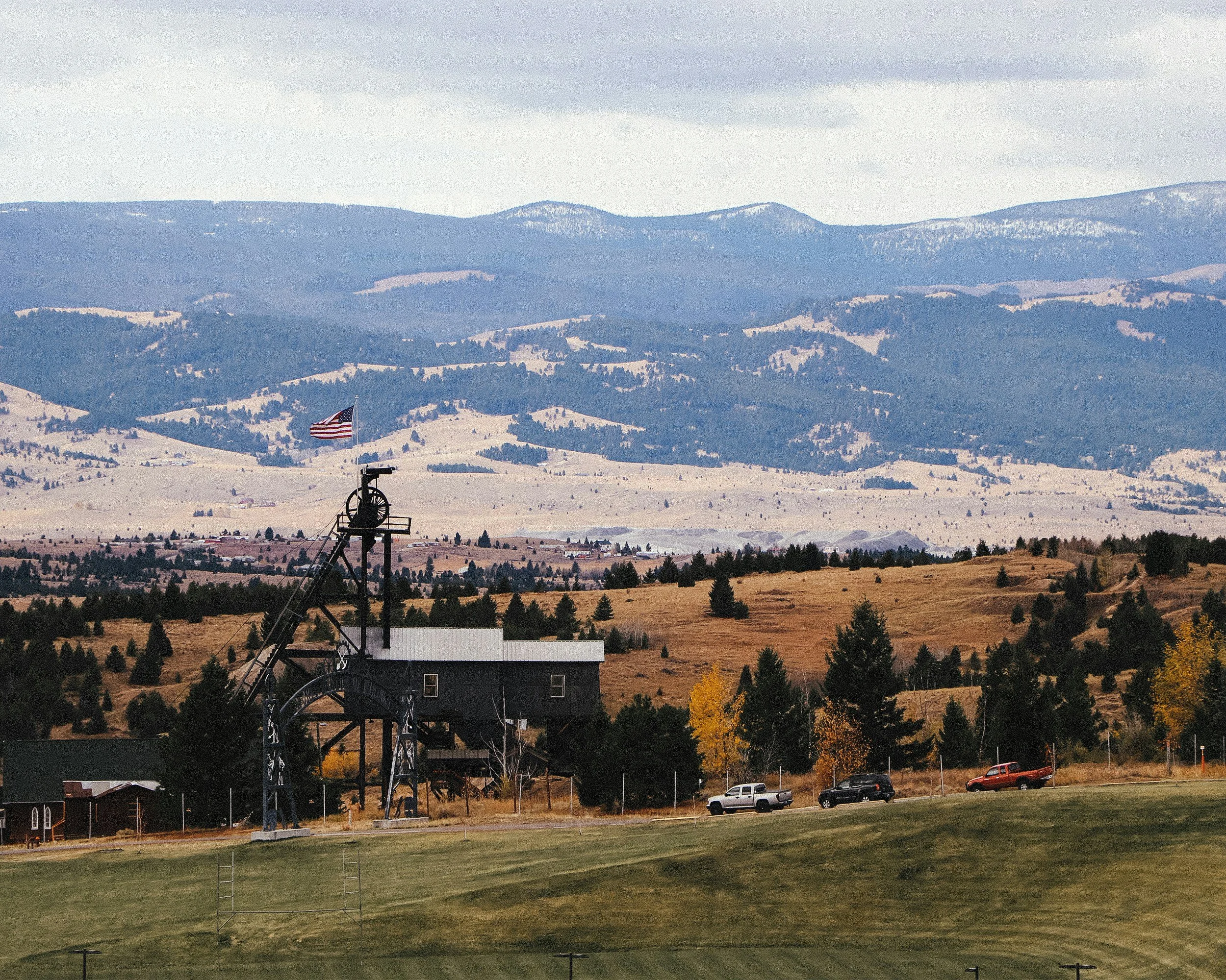 Scenic rural landscape with a Montague wheel and a flag, rolling hills, and mountains in the background.