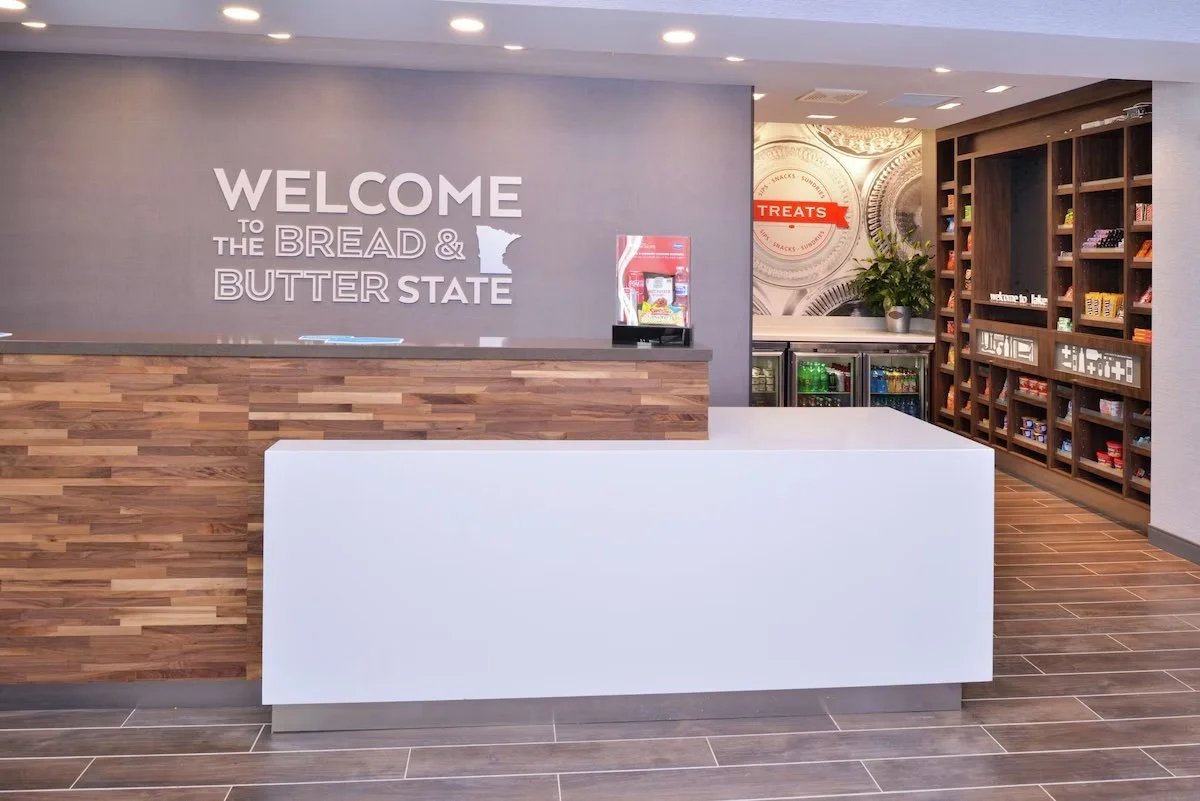 Museum or visitor center reception desk with welcome sign that reads 'Welcome to the Bread & Butter State,' with shelves of snacks and treats in the background.