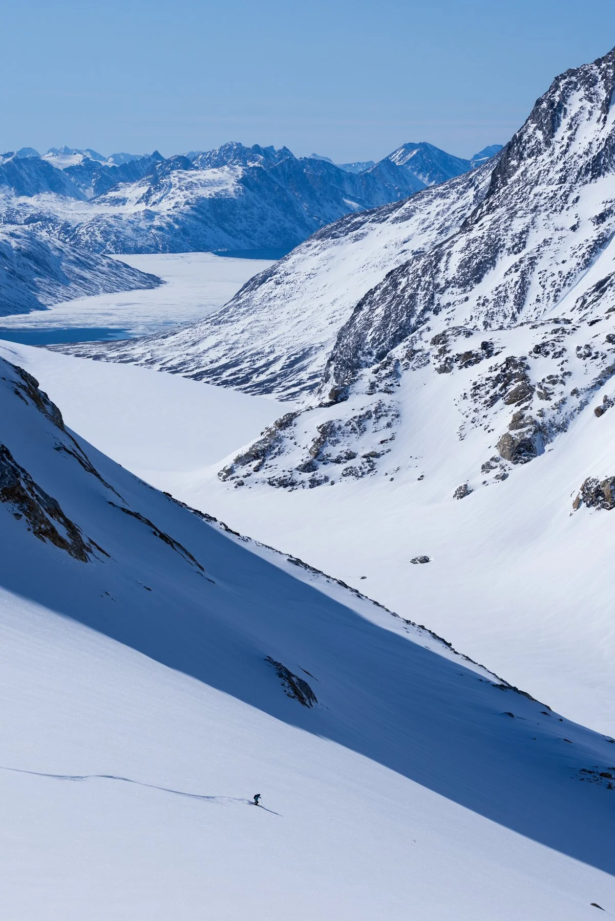 Berglandschaft mit schneebedeckten Bergen, Gletschern und einem Skifahrer im Vordergrund.