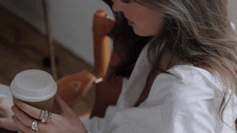 Woman in a white shirt holding a disposable coffee cup with a white lid.