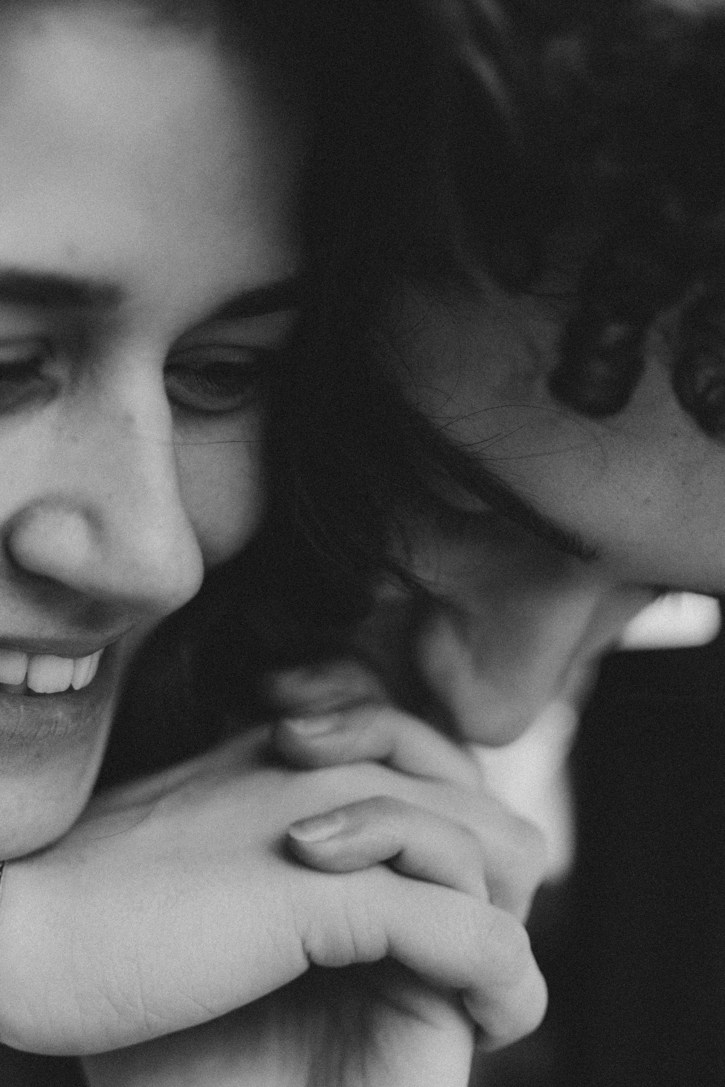 Close-up of a happy couple smiling, with their heads together, showing their faces and hands in black and white.