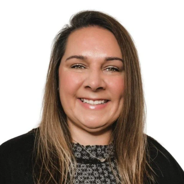 Smiling woman with long brown hair wearing a black top with a patterned collar, against a white background.