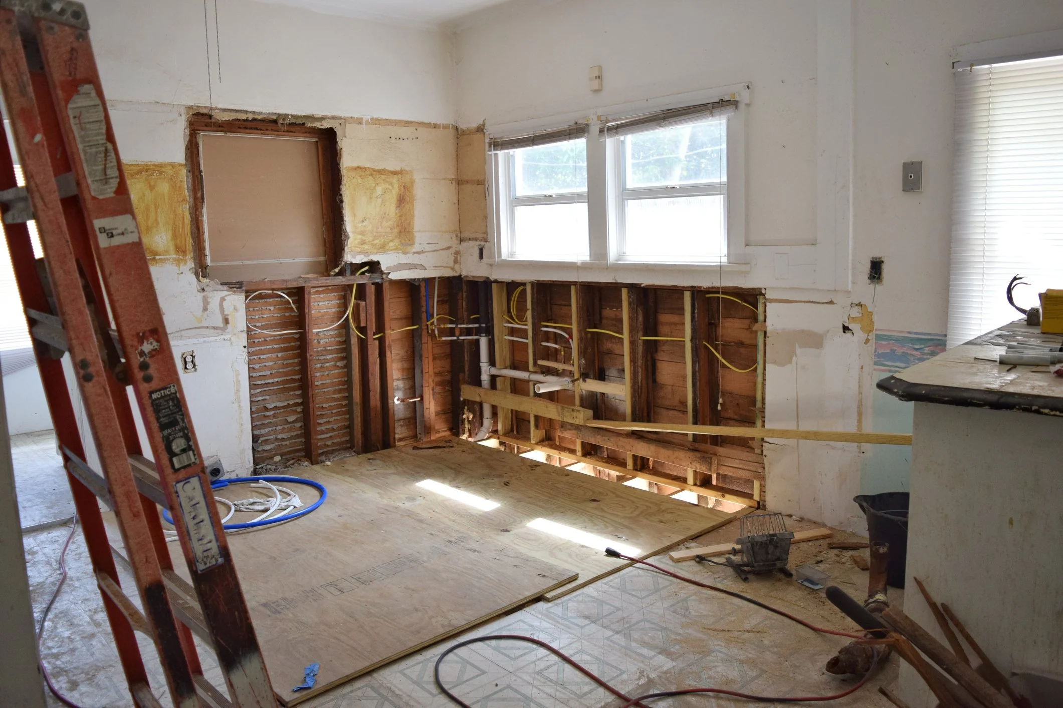 Room under renovation with removed wall, exposed electrical wiring, window, and construction tools.