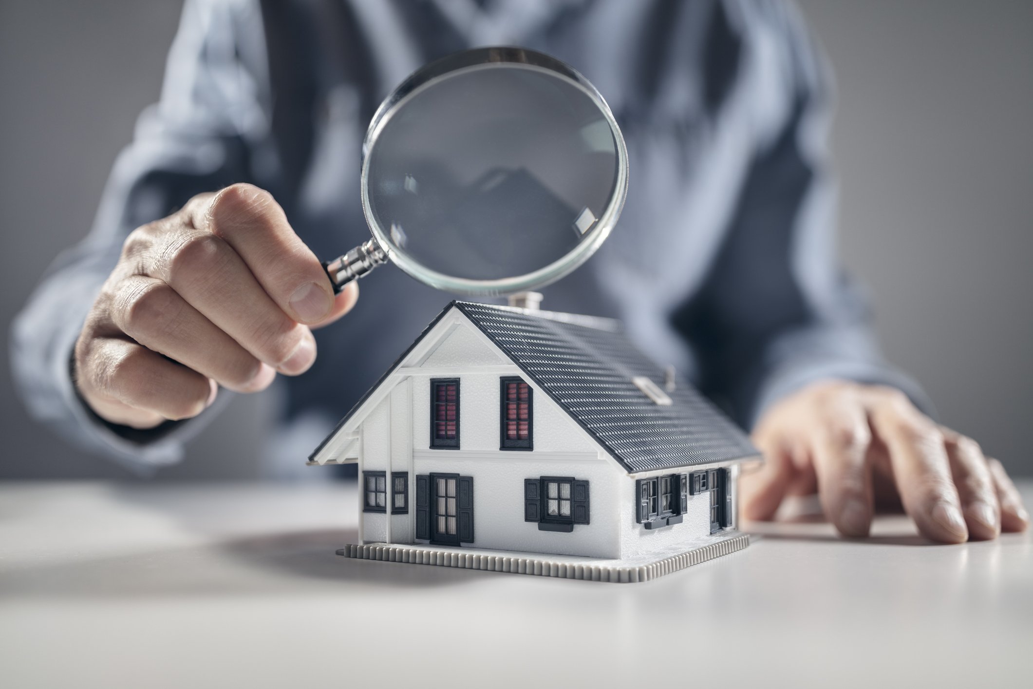 Person examining a model house with a magnifying glass.
