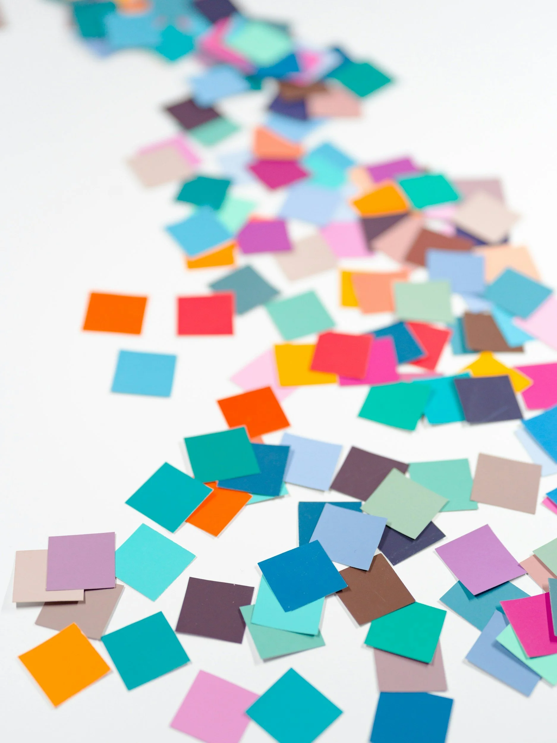 Colorful confetti square-shaped paper pieces scattered on a white surface.