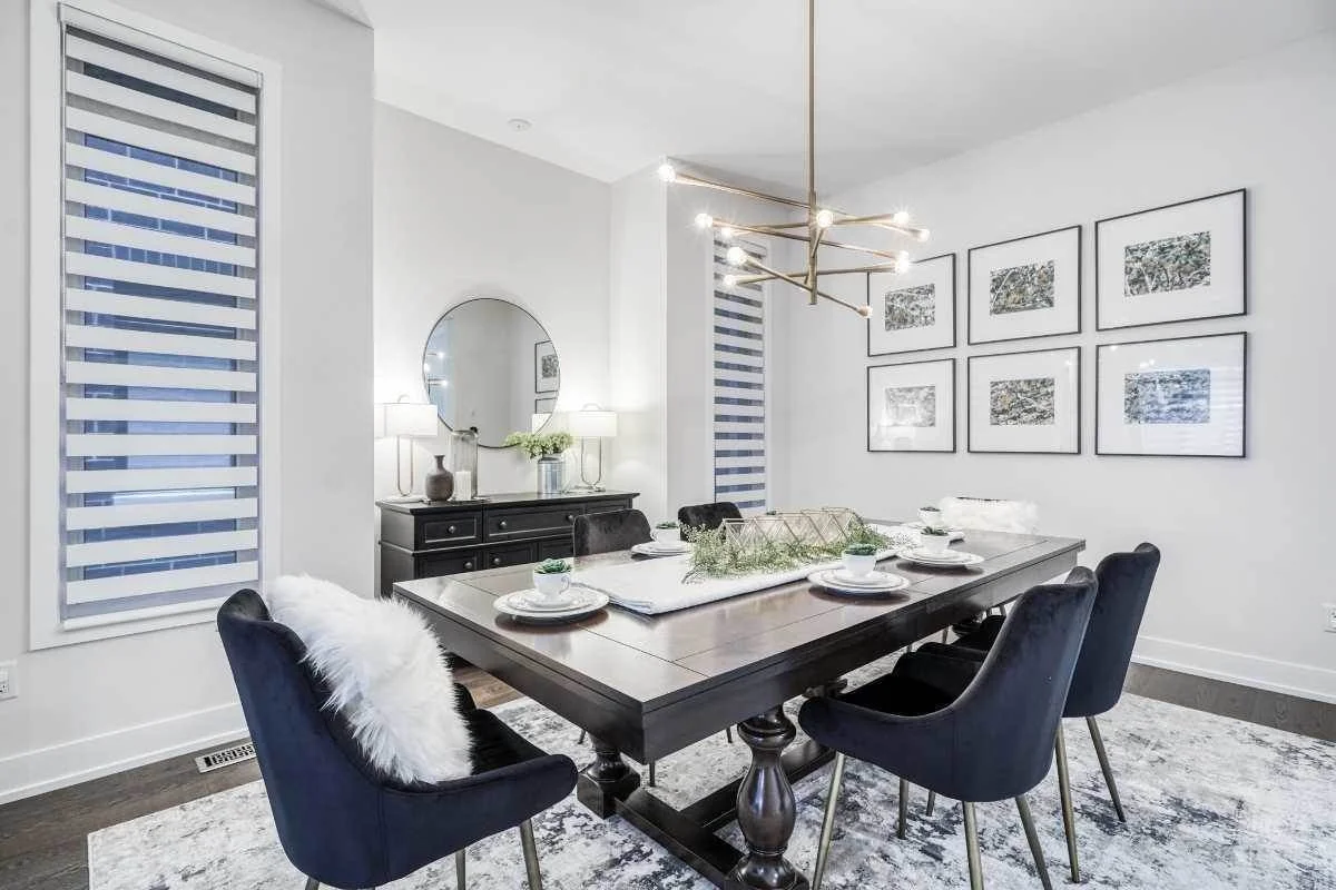 Modern dining room with black dining table, six black chairs, white walls, wall art, black sideboard, round mirror, and decorative lighting fixture.