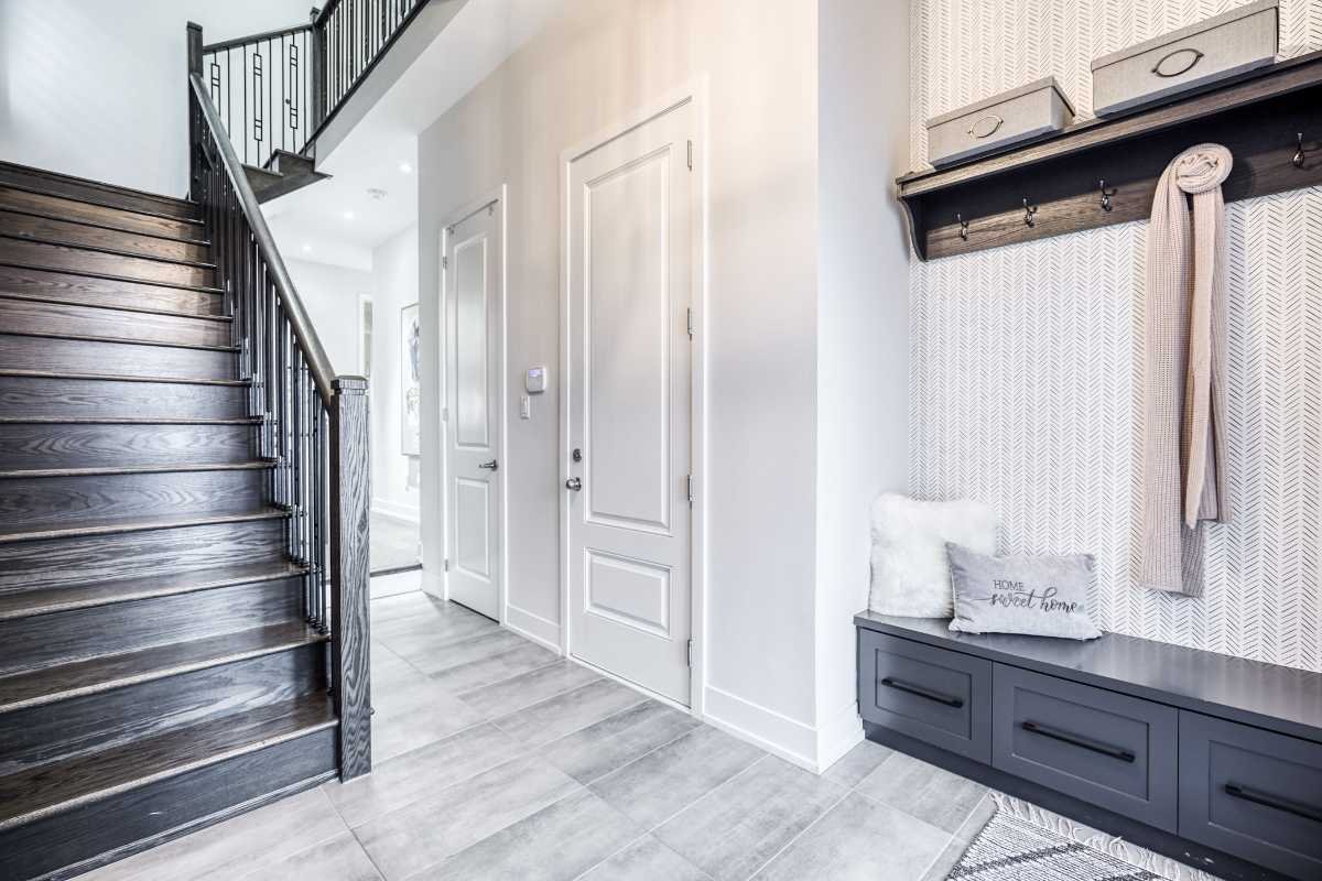 Entryway with staircase, white walls, closed white doors, wooden and gray storage bench with cushions, and wall hooks for coats.