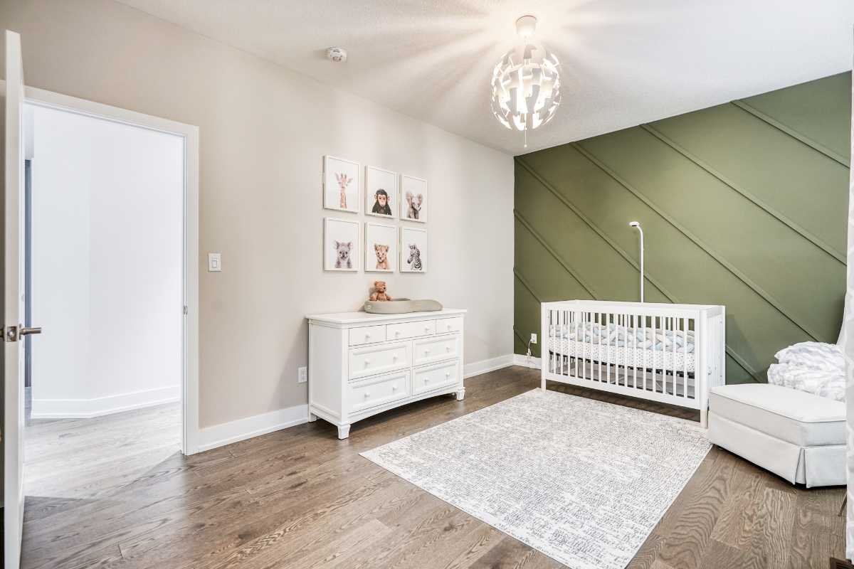 Baby crib, changing table, and armchair in a nursery room with hardwood floors, green accent wall, and wall art of animals.