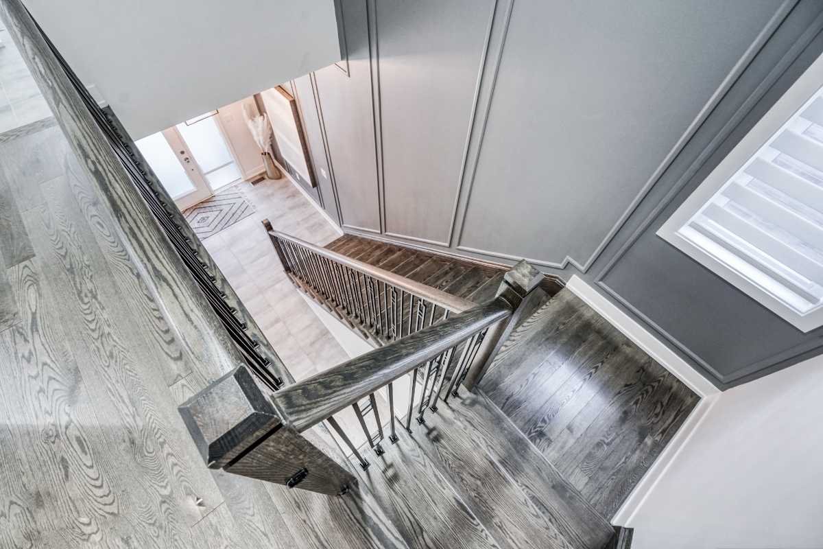 Overhead view of a staircase with dark wood handrail and metal balusters inside a home with light-colored wood flooring and gray walls.