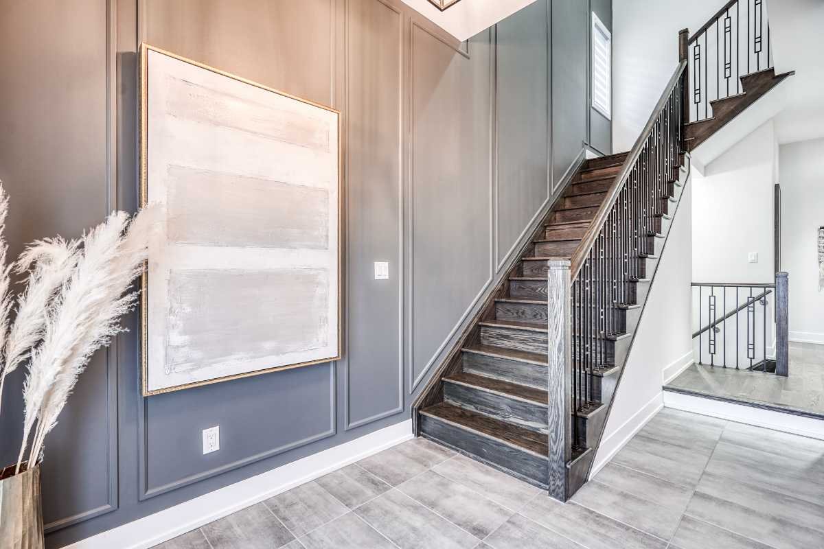 Interior of a modern home entryway with gray walls, a large abstract painting, and a dark wood staircase with black railing.