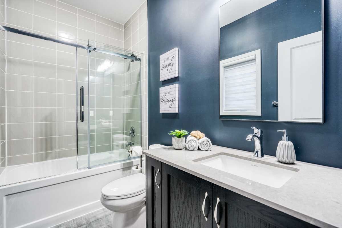 Modern bathroom with a bathtub and shower, dark blue wall, white countertop vanity with a sink, mirror, and decorative items such as towels and a small plant.