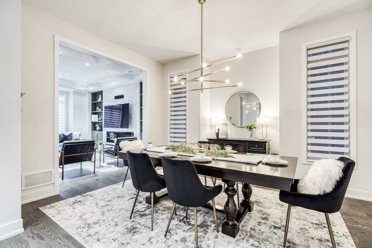 Modern dining room with a dark wood table, black chairs, and white tableware, with a large round mirror and two table lamps on a black sideboard in the background.