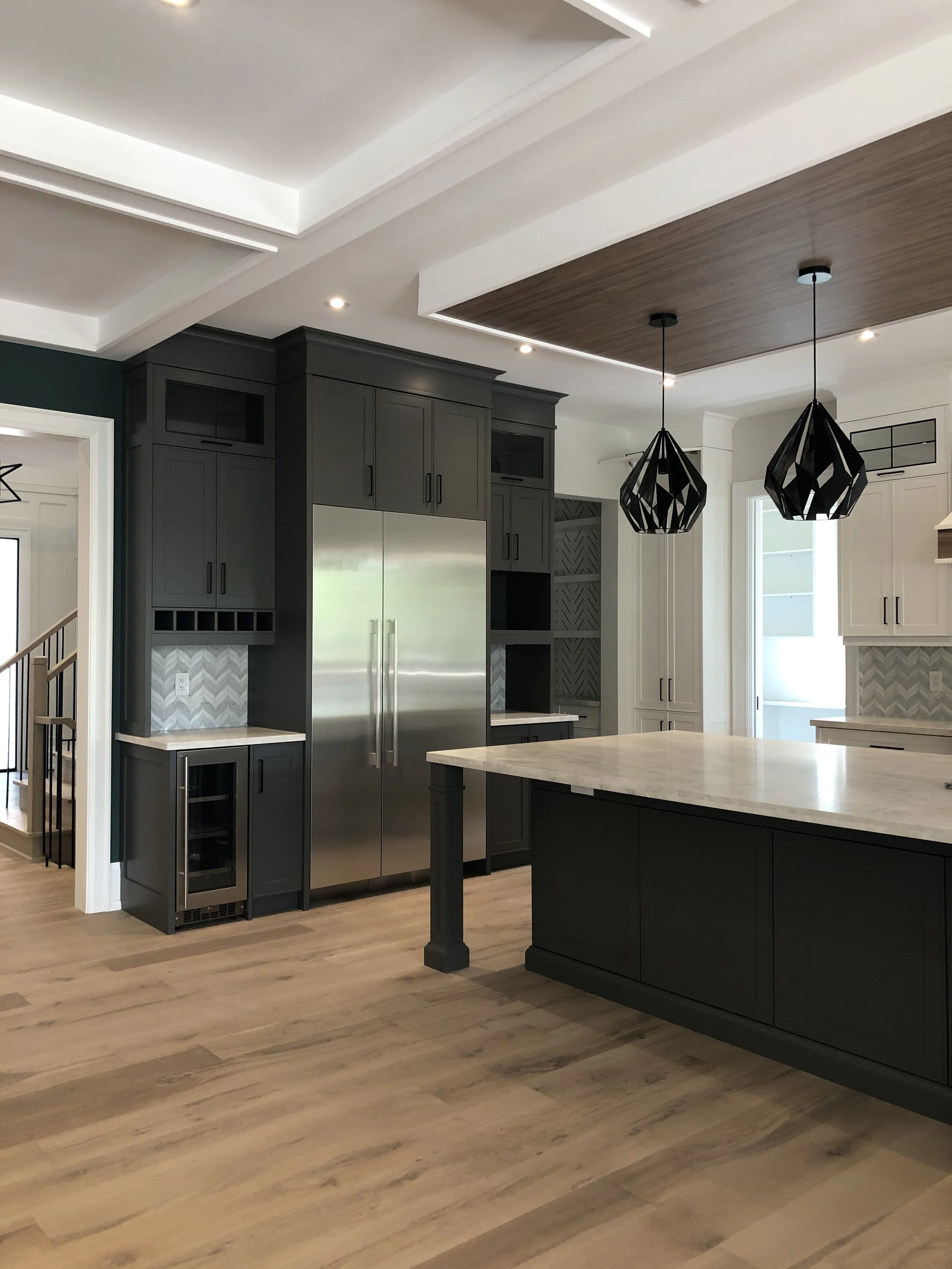 Modern kitchen with dark gray cabinets, a large stainless steel refrigerator, a marble island, black pendant lights, and wood flooring.