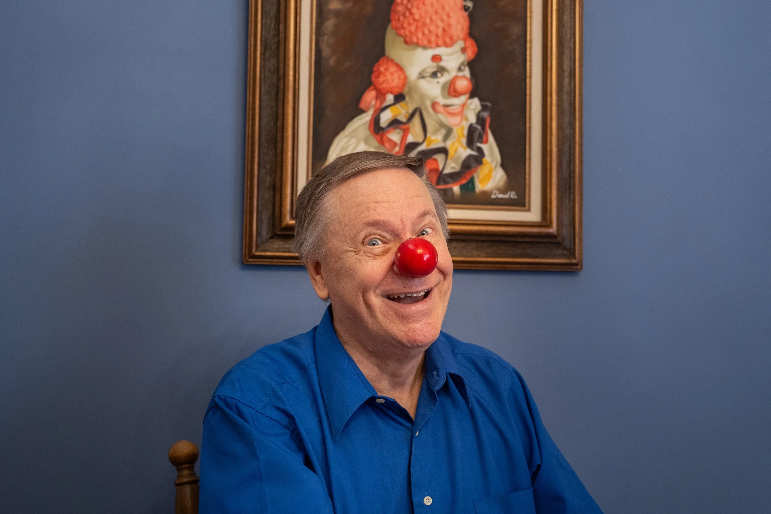 Randall Munson, also known as "Circles the Clown," poses for a picture under a portrait of him in costume at his home in Rochester on Thursday, Aug. 7, 2025. (Post Bulletin)