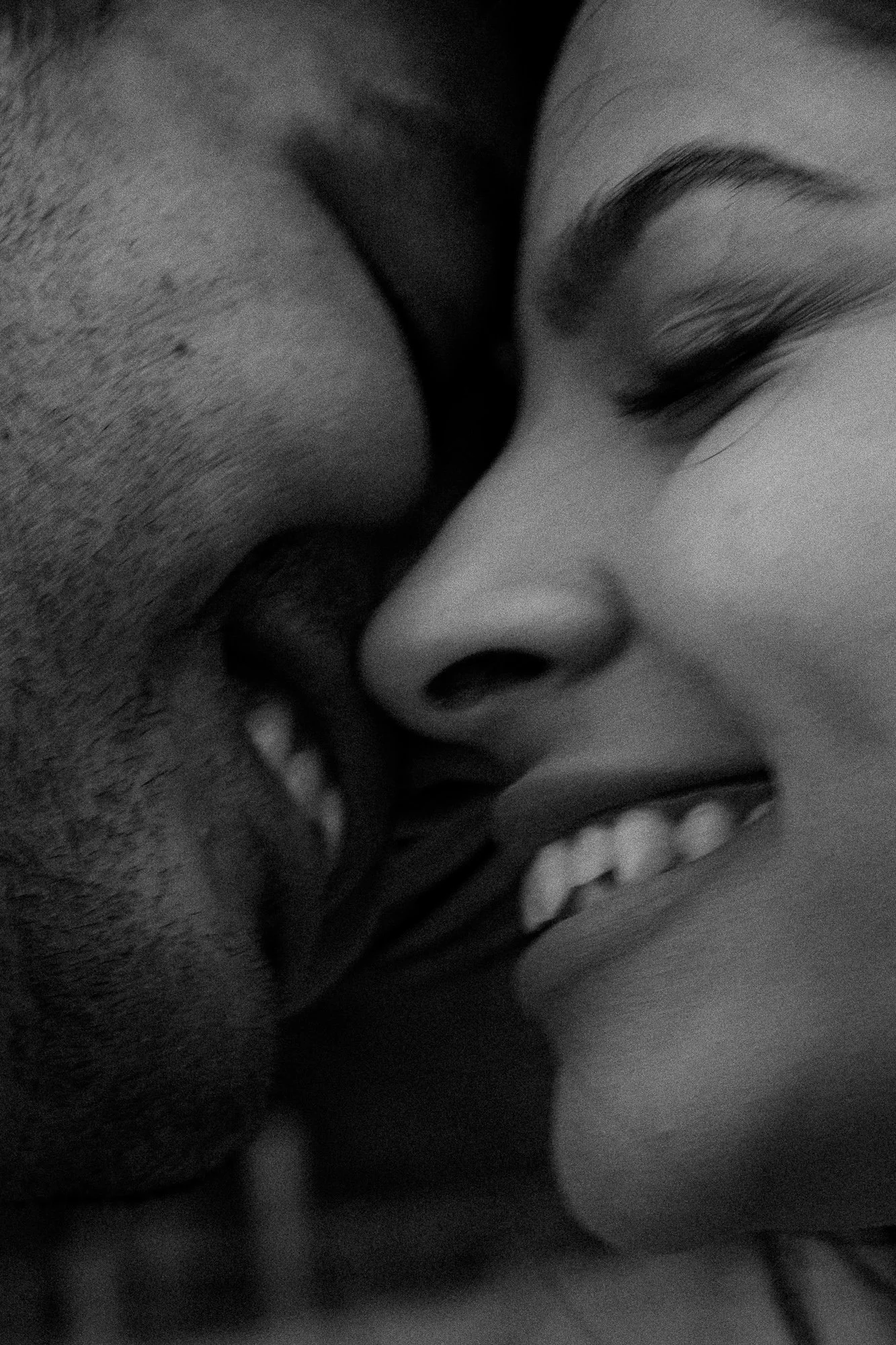 Close-up of two people smiling and touching noses, with their faces close together, in black and white.