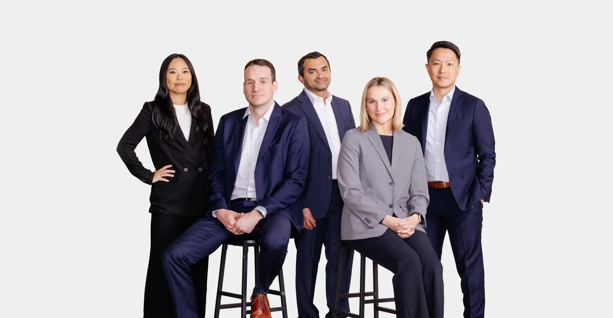 Group of five diverse professionals in business attire posing against a plain white background.