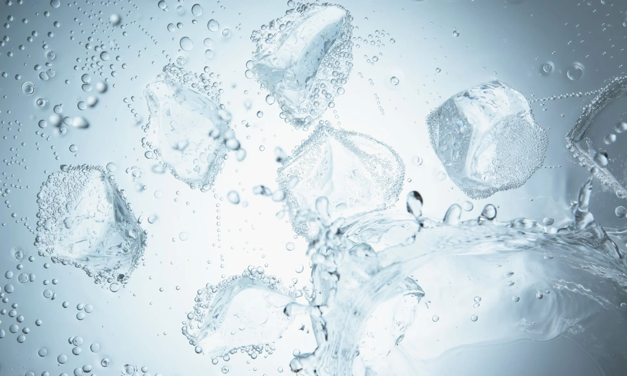 Ice cubes splashing into water with bubbles and droplets surrounding them.