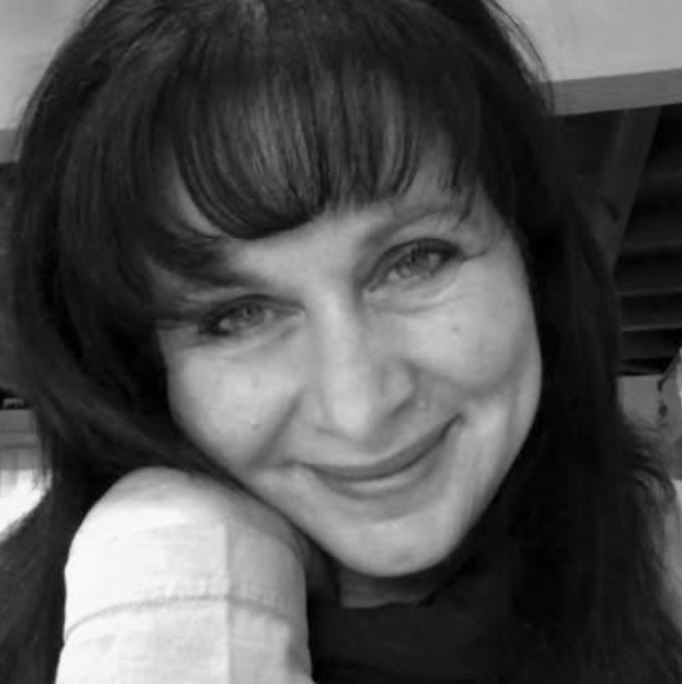 A woman with dark hair smiling, resting her chin on her arm.