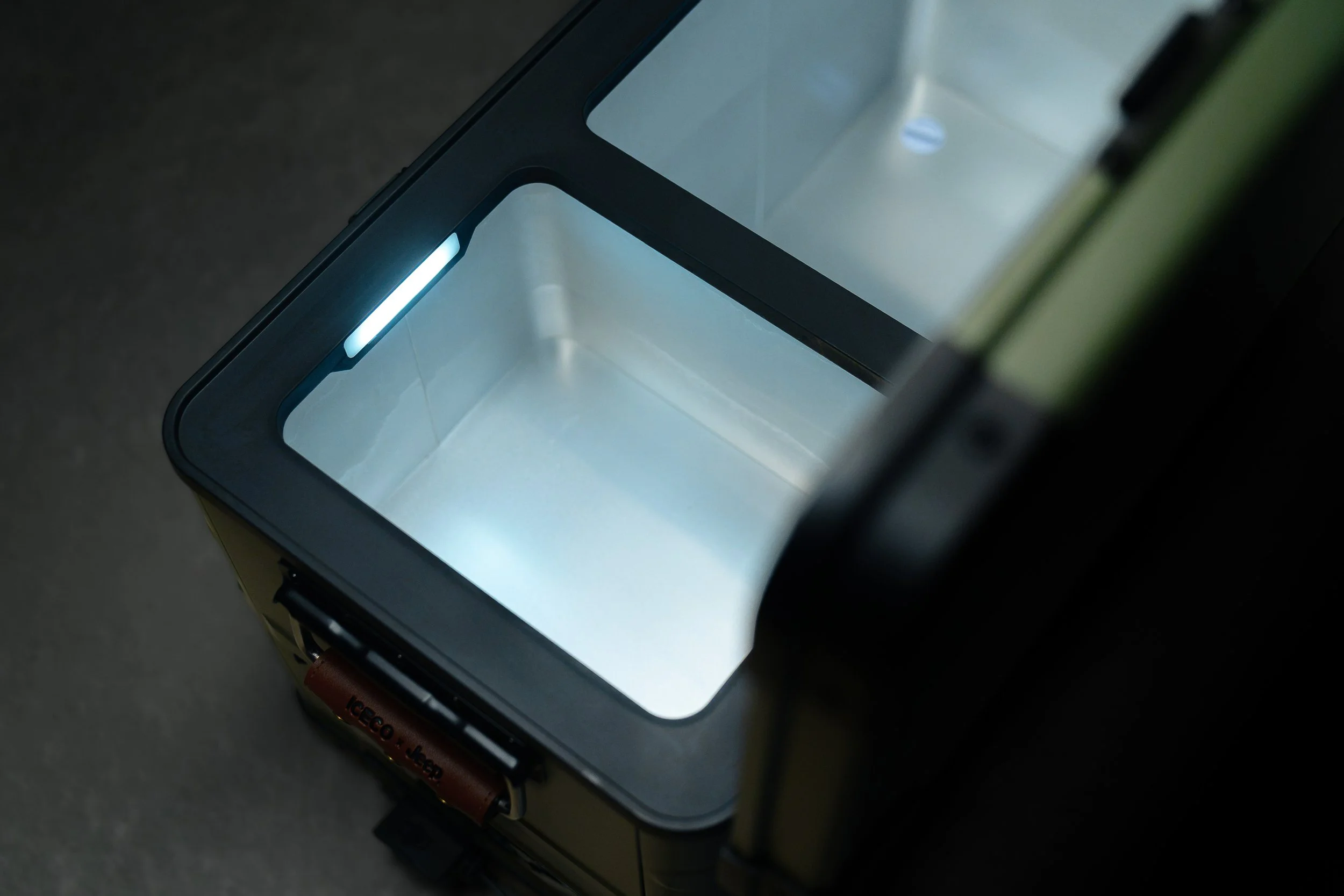 A tabletop oven or toaster oven with a glass door, showing a bright interior light and an empty cooking chamber, positioned on a dark surface.
