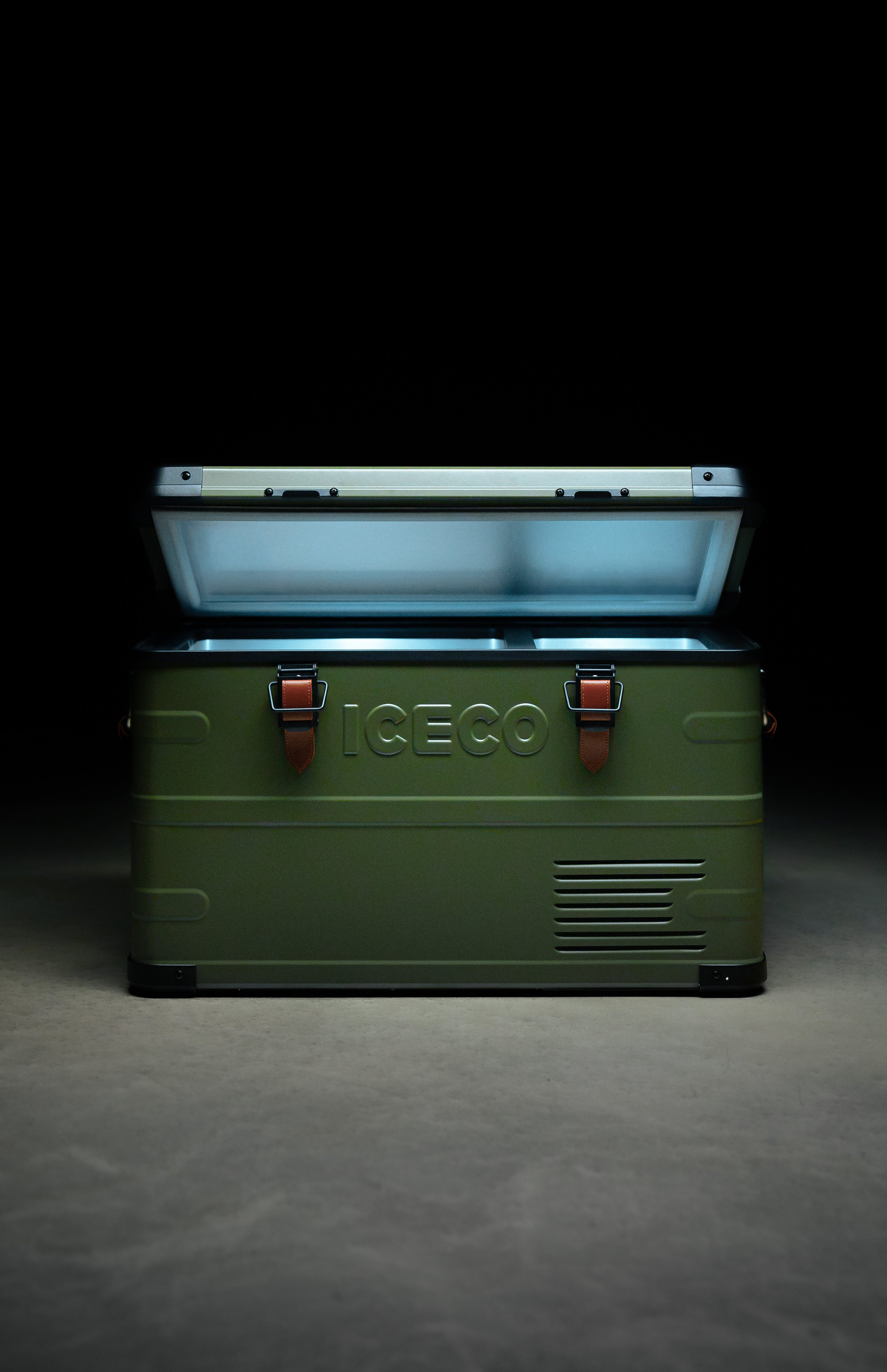 A green insulated cooler with the brand name 'ICECO' embossed on the front, placed on a gray concrete surface, with a black background.