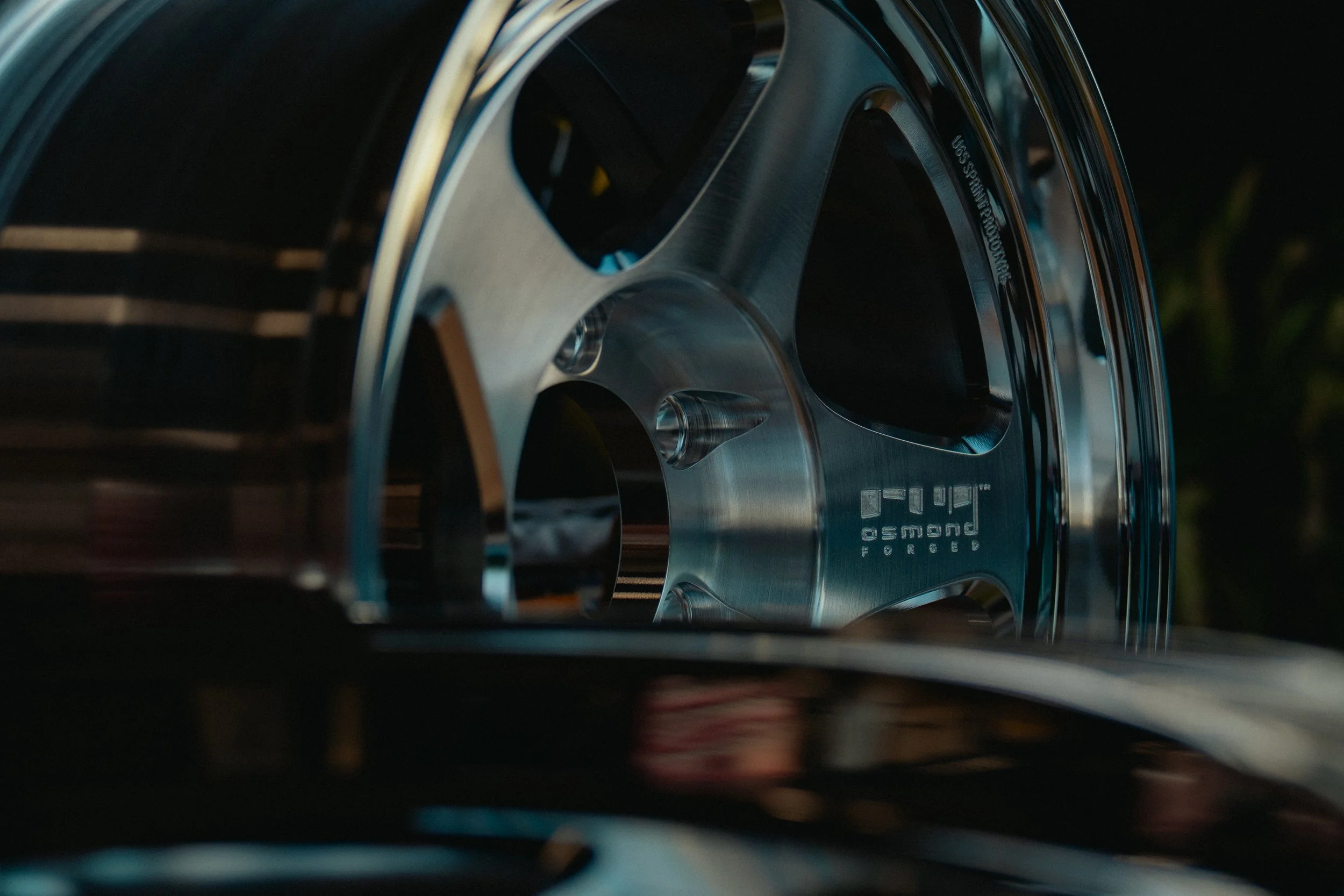 Close-up of a Porsche wheel rim with the Porsche logo visible, shot at an angle with reflections on the metal.