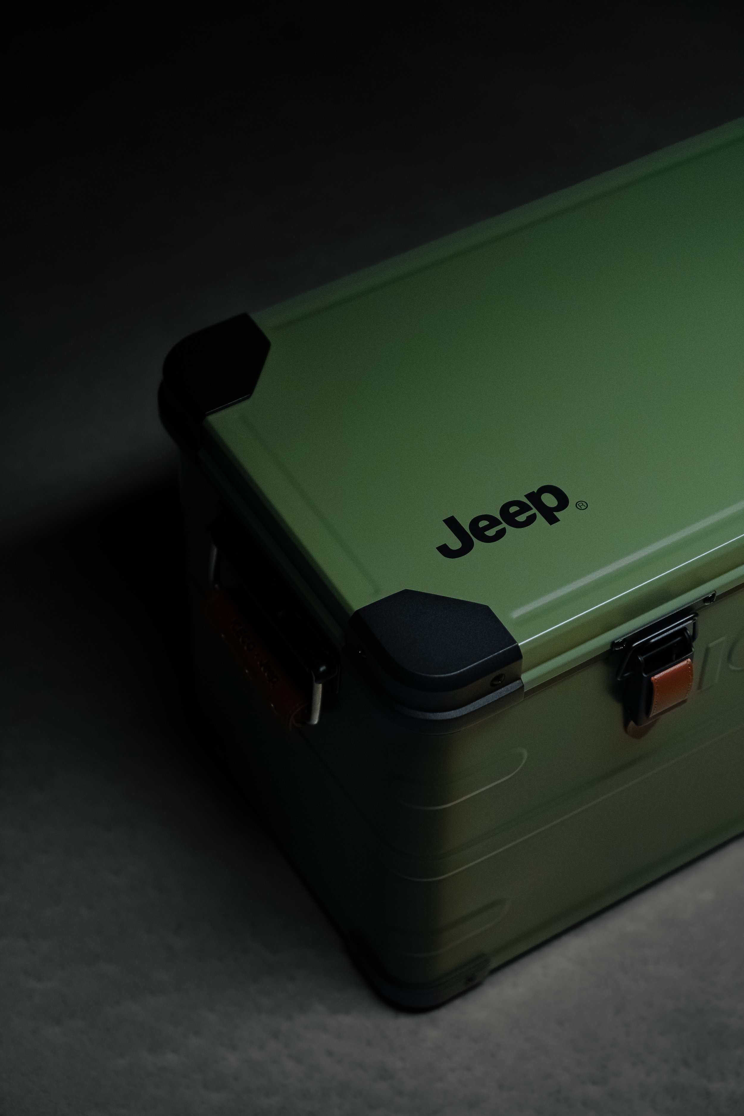 Close-up of a green Jeep vehicle with black accents, showing part of its lid and corner.