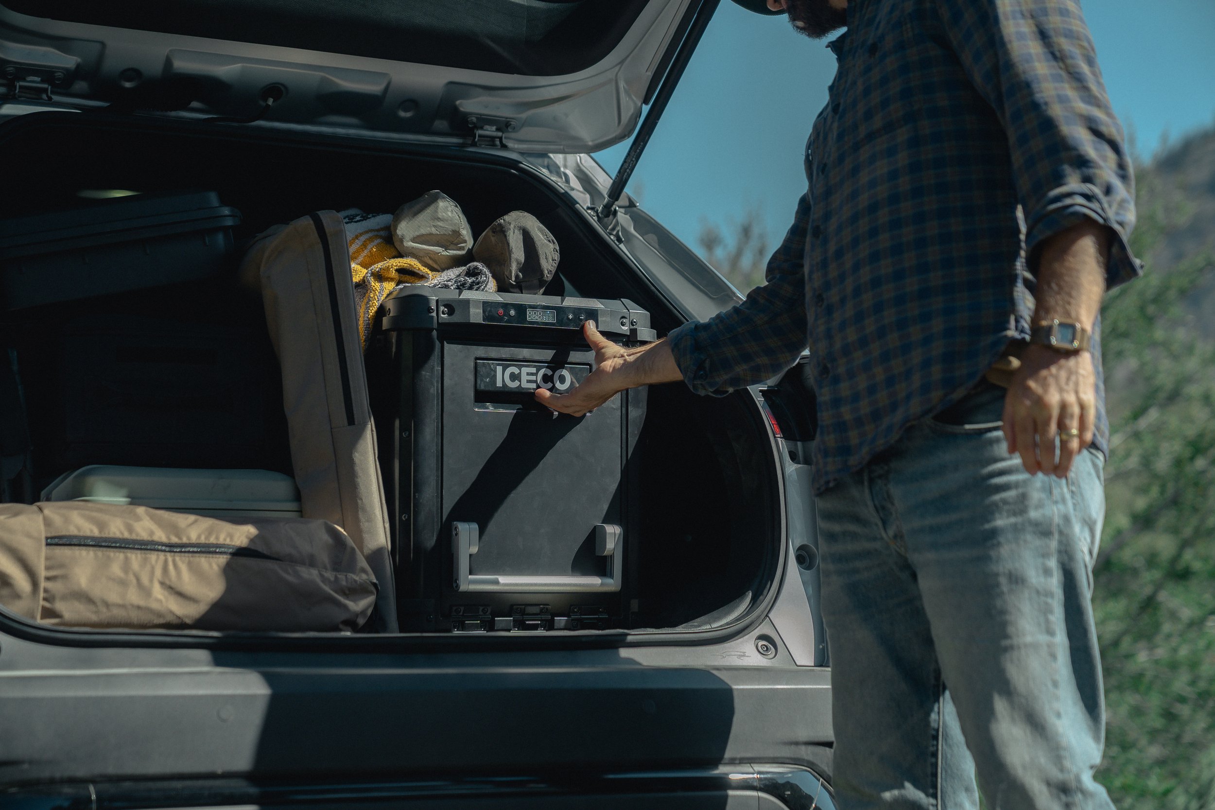 Person opening the trunk of a vehicle, revealing camping gear and an ICECO portable refrigerator.