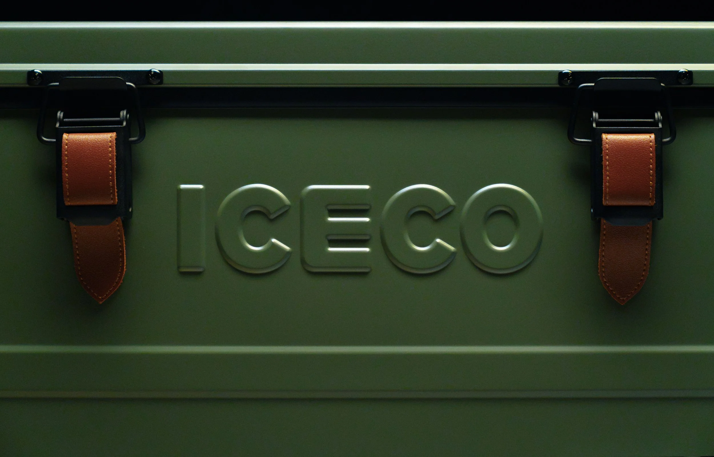 Close-up of a green vintage metal storage box with embossed letters and brown leather straps.