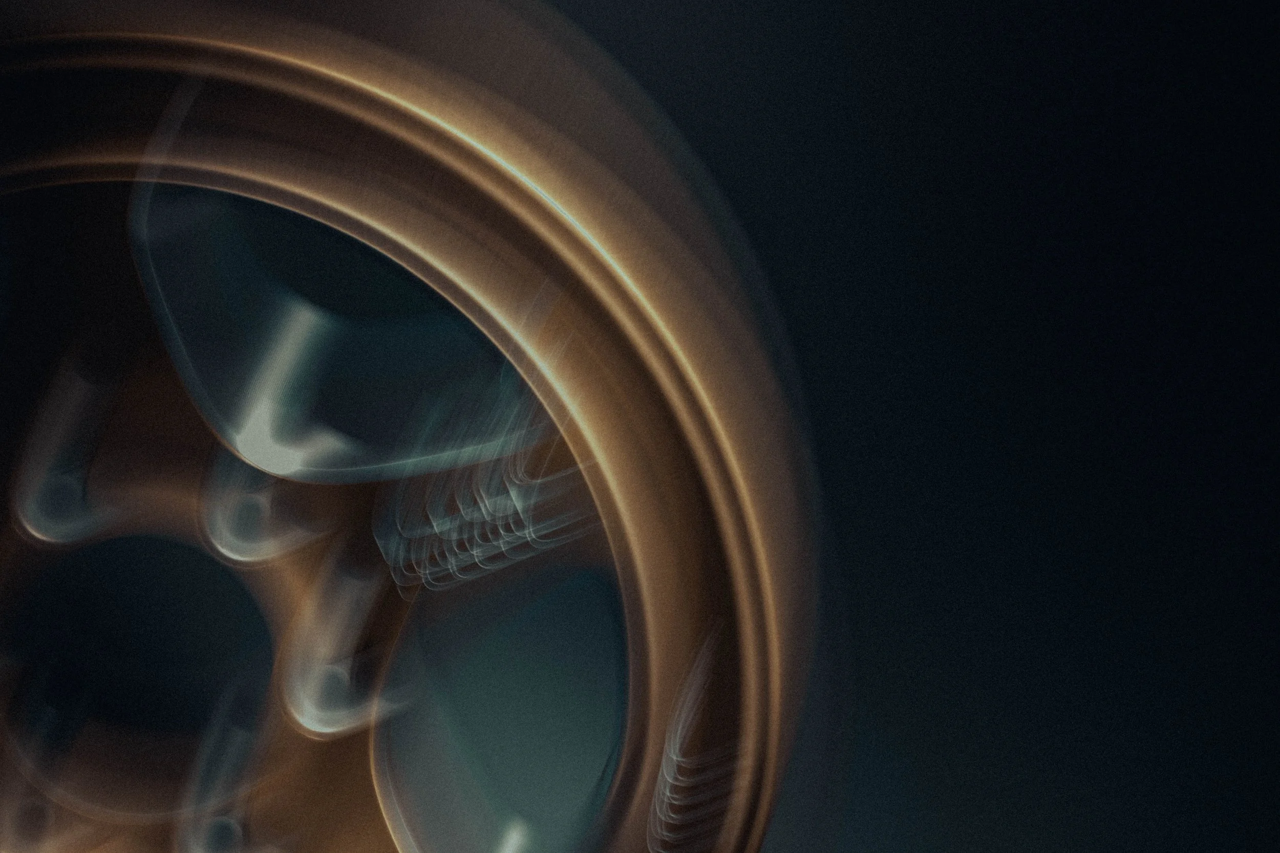 Abstract image featuring blurred golden and blue lines creating circular and wavy patterns on a dark background.