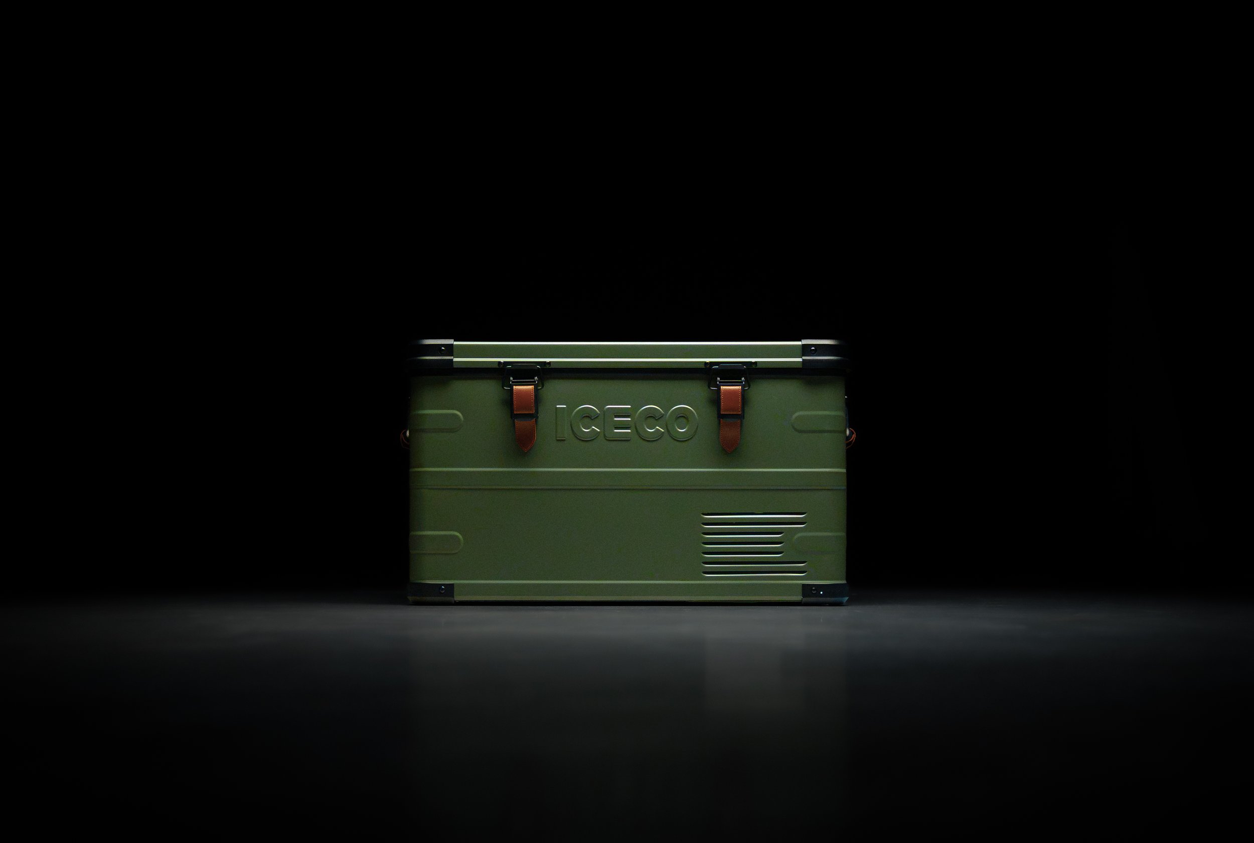 A green portable cooler with brown leather straps and the word "ICECO" embossed on the front, set against a black background.
