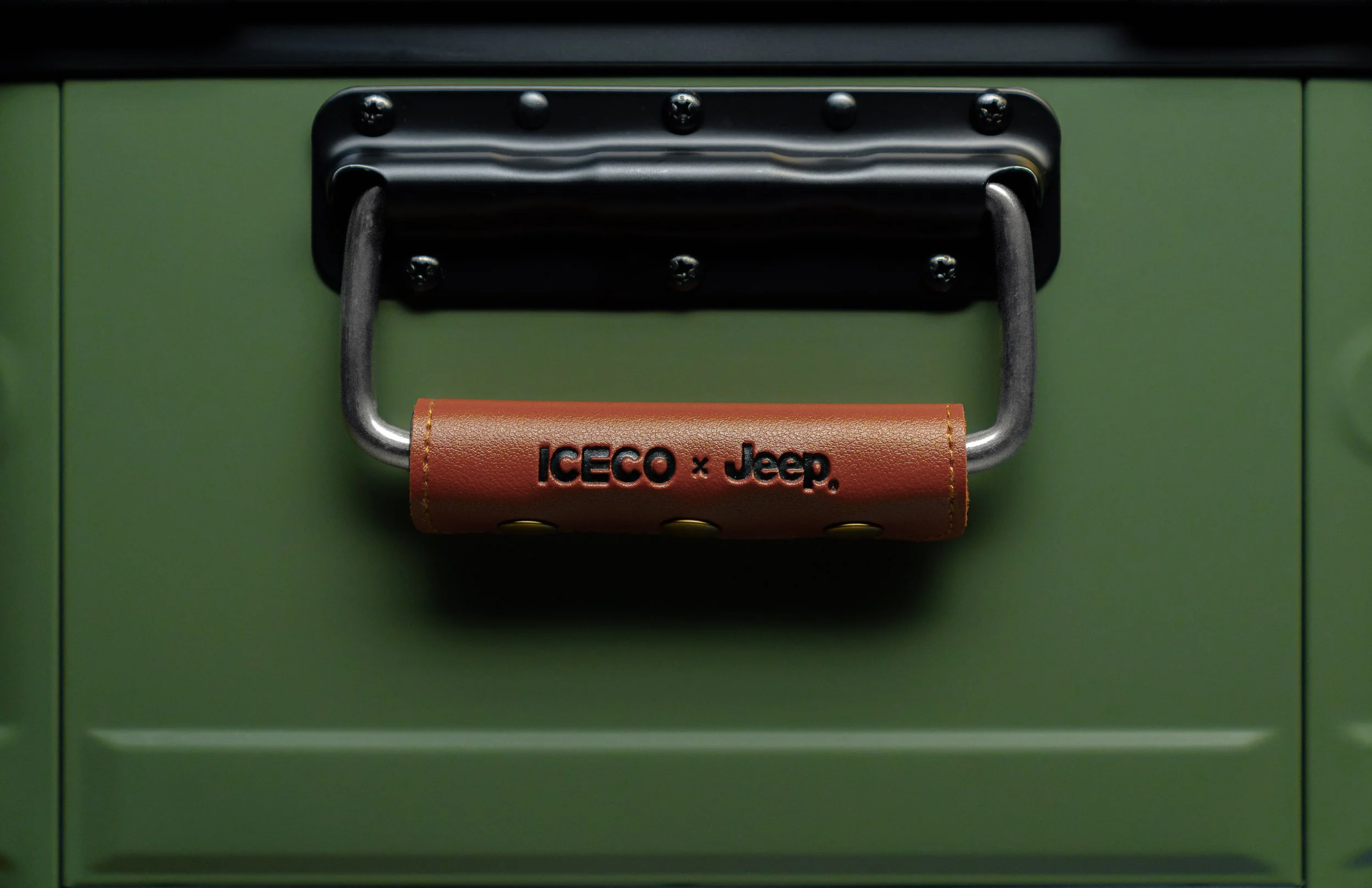 Close-up of a metal latch on a green door with a padded leather handle that has the text 'ICECO x Jeep' on it.