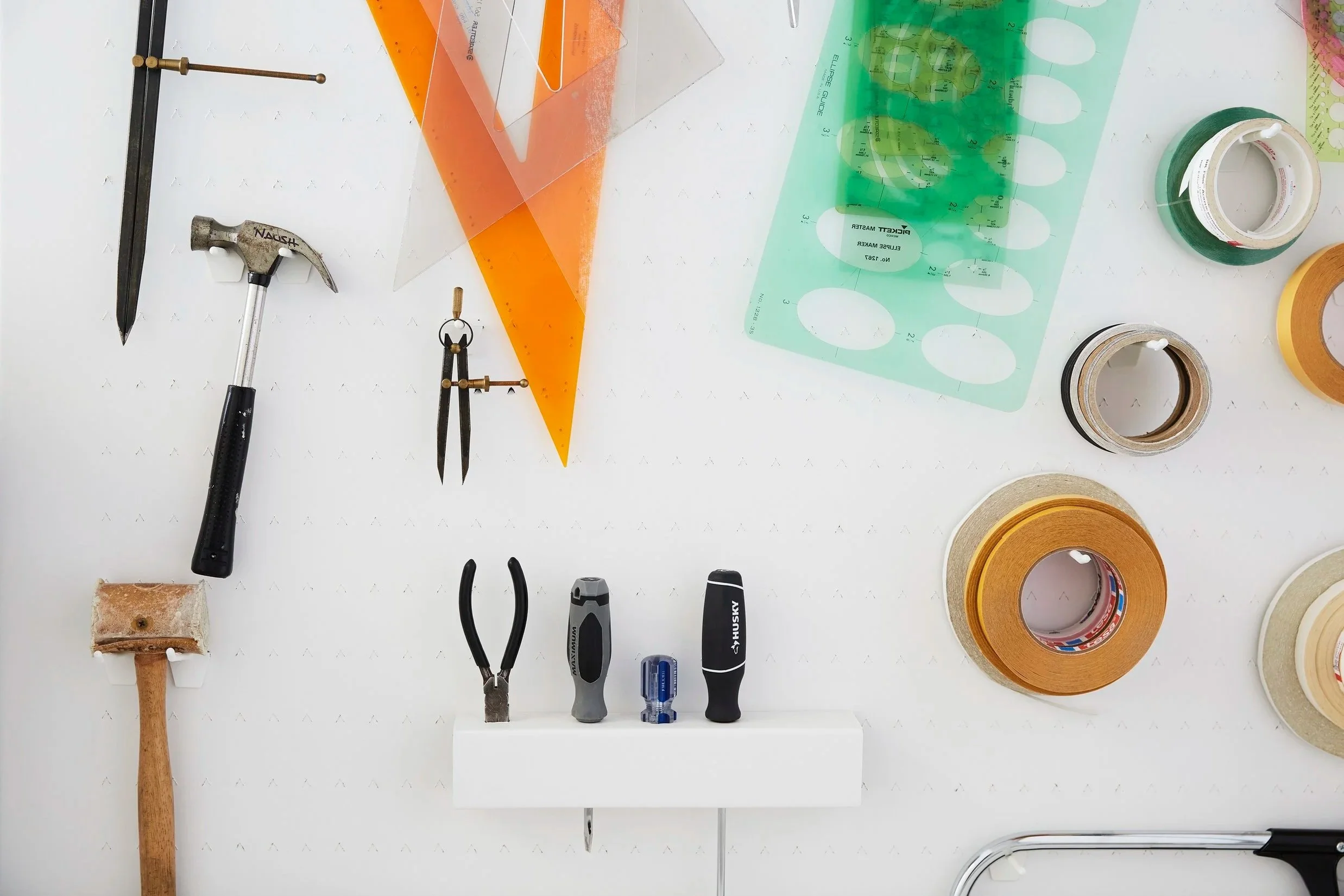 Proprint production tools and supplies arranged on a white wall, including measuring templates, hand tools and rolls of tape used in commercial printing.