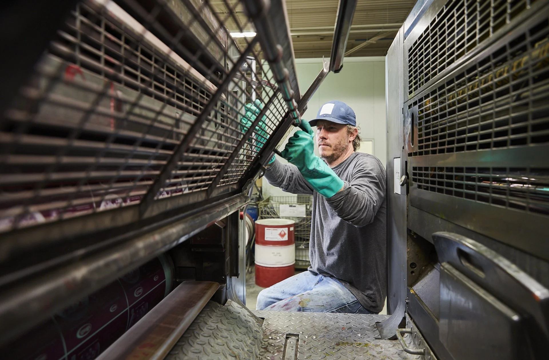 Proprint production employee wearing protective gloves while inspecting and adjusting industrial printing machinery, surrounded by the equipment's metal framework.
