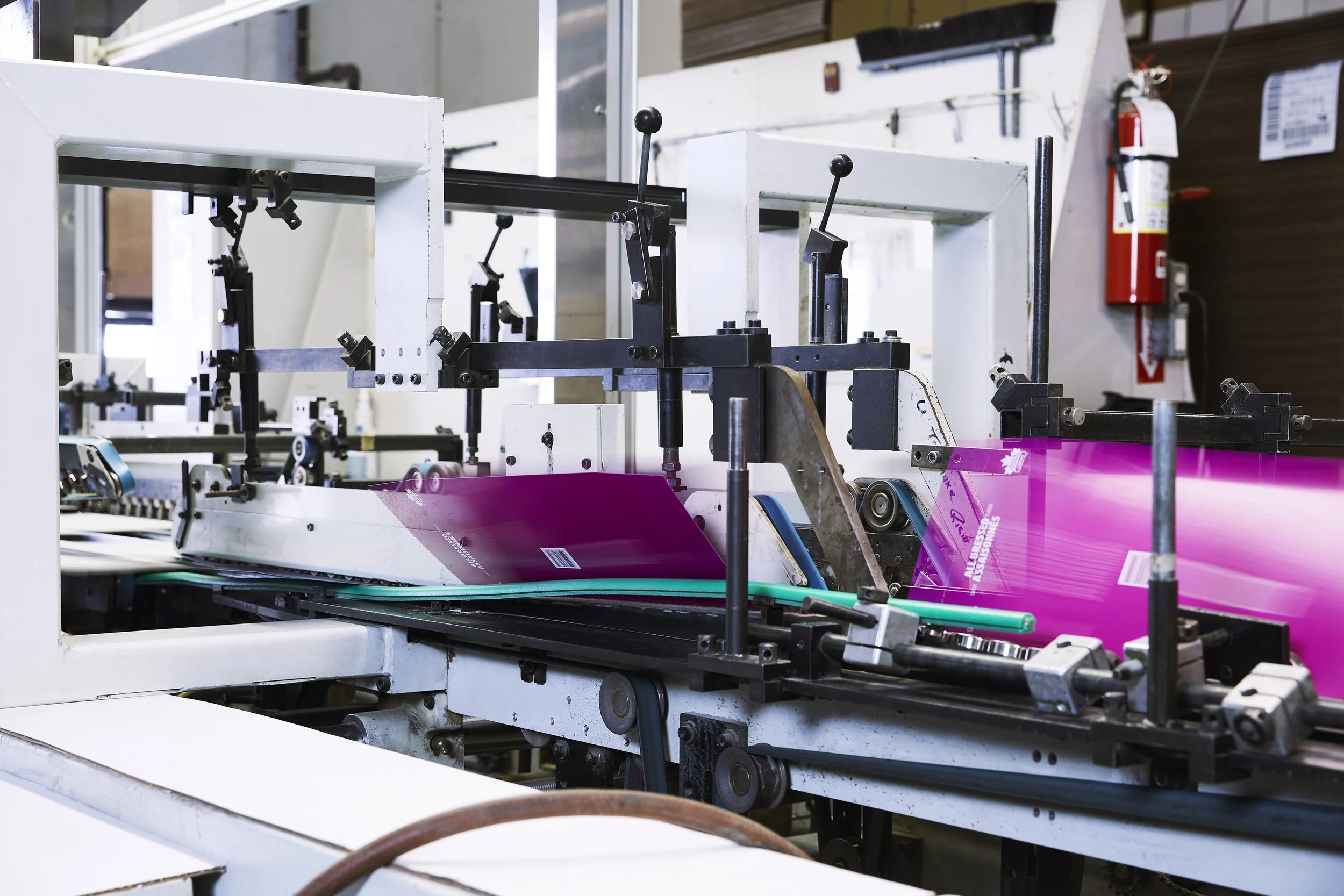 Proprint brand photography showcasing industrial printing equipment processing vibrant magenta printed materials, highlighting the company's commercial printing capabilities.