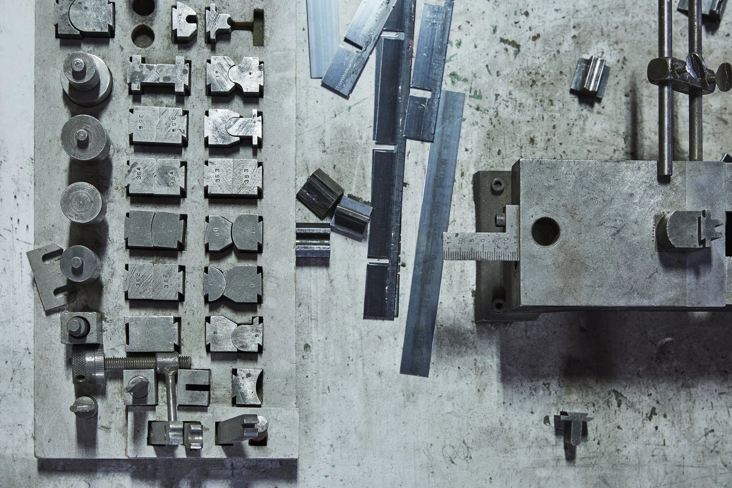 Overhead view of assorted metal printing components, measuring tools and mechanical parts arranged on a well-used industrial workbench at Proprint.