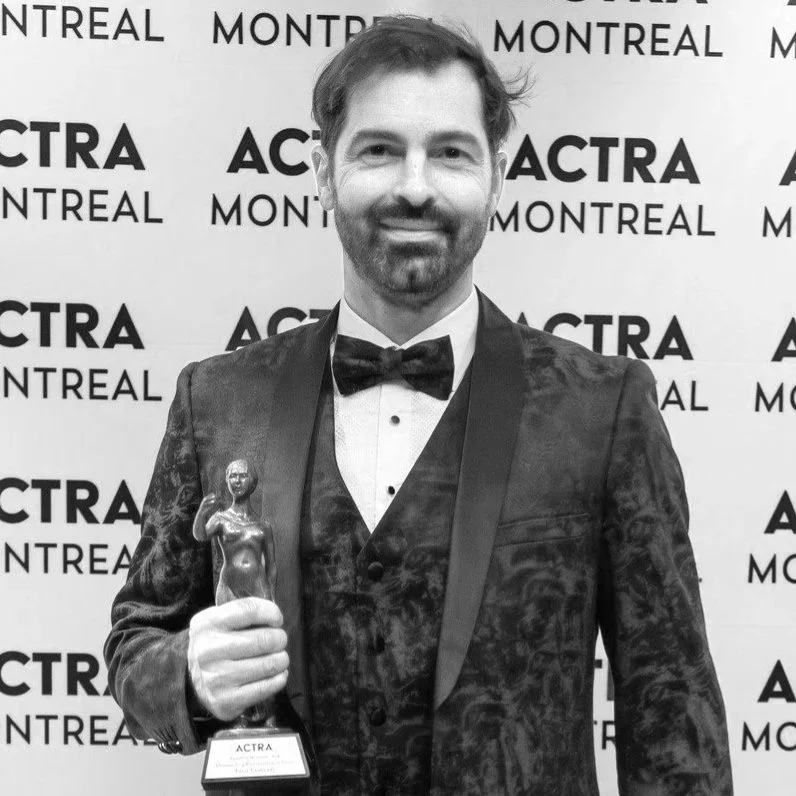 A man in a tuxedo holding an award trophy at an event with a backdrop that says ACTRA Montreal.
