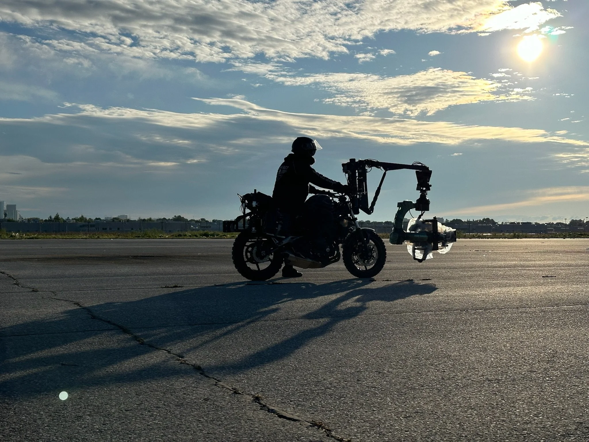 Silhouette of a person riding a motorcycle on an empty road during sunset or sunrise with clouds in the sky.