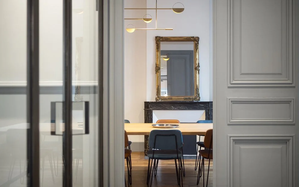 Salle de réunion avec un miroir doré agencé au-dessus d'une cheminée en marbre noir, vue à travers une porte vitrée.
