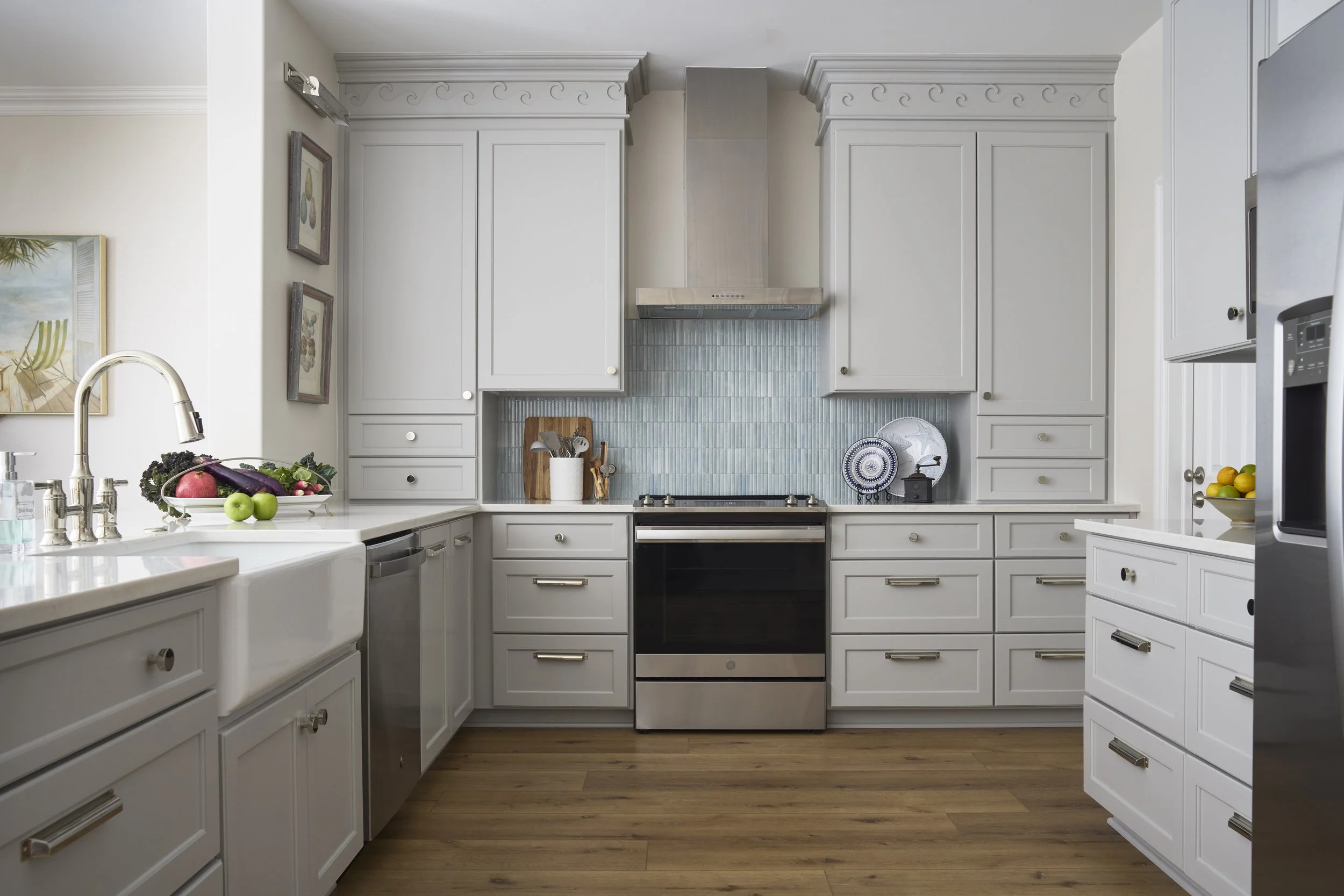 Modern kitchen with gray cabinets and nickel hardware, stainless steel appliances, wooden floor, fruit and vegetables on the counters.