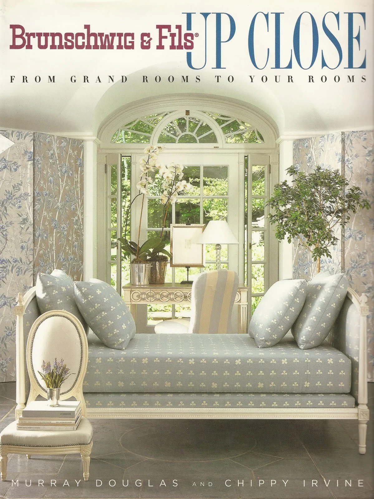 Book cover for 'Up Close: From Grand Rooms to Your Rooms' by Murray Douglas and Chippy Irvine, featuring a bright, cozy sunlit conservatory with floral patterned upholstery, a small side table with books, a potted orchid, and indoor plants.