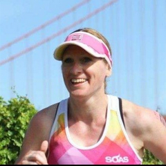 A woman with wavy light brown hair smiling outdoors against a blue sky.