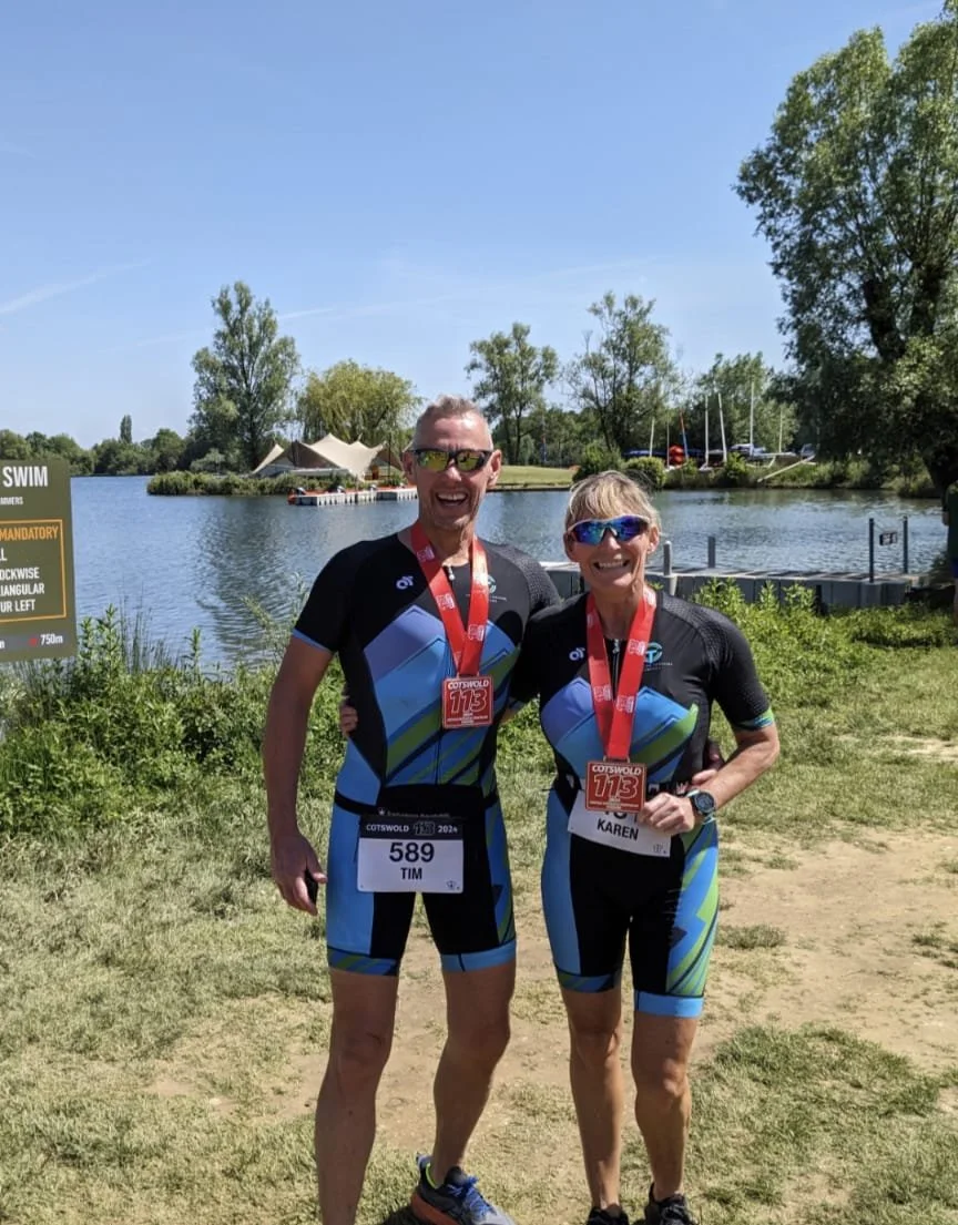Two TCC athletes holding their race medals beside a lake