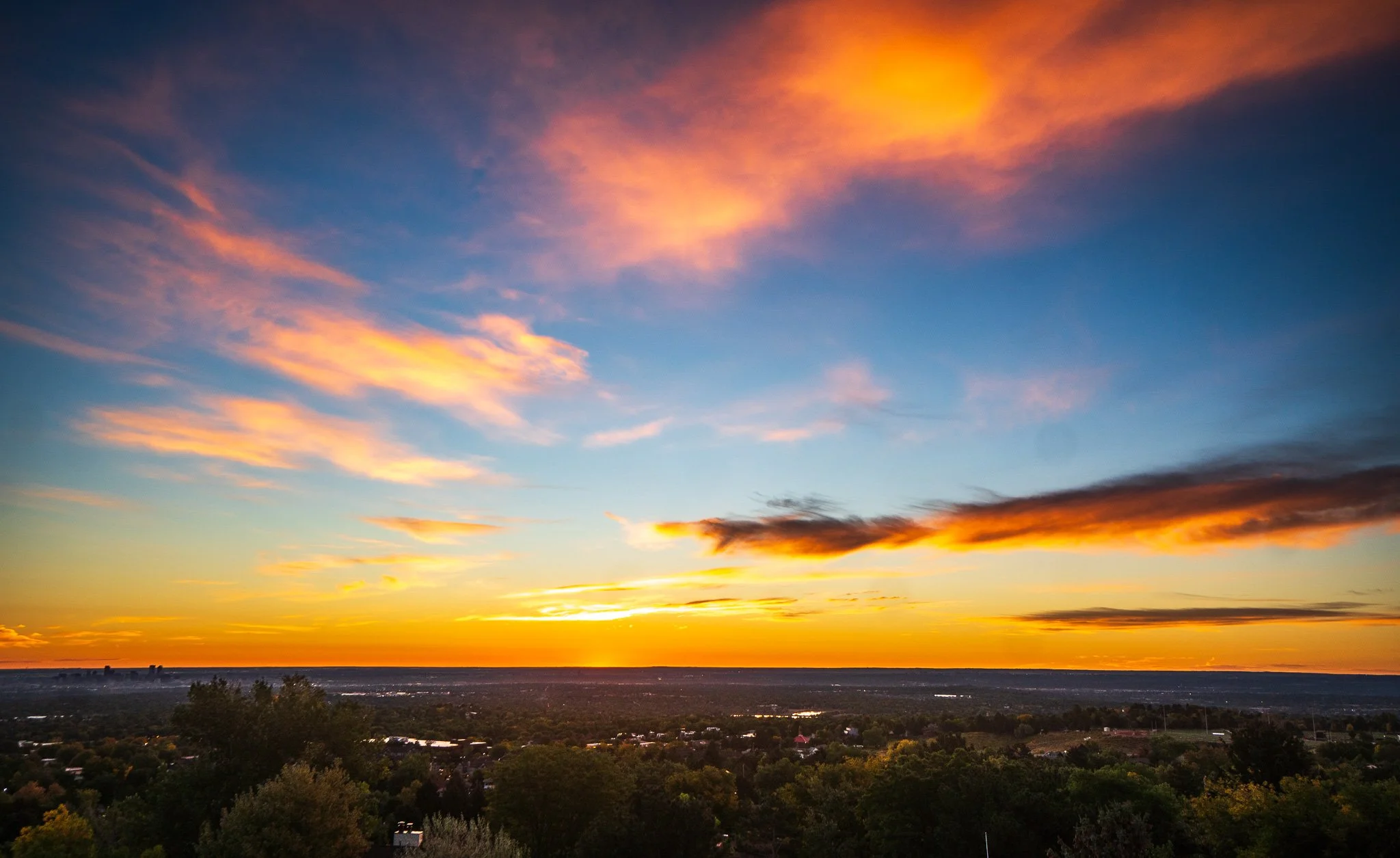 The colorful sunset view on the Sky Deck at Denver Skyline Venue with trees and a distant Denver skyline.