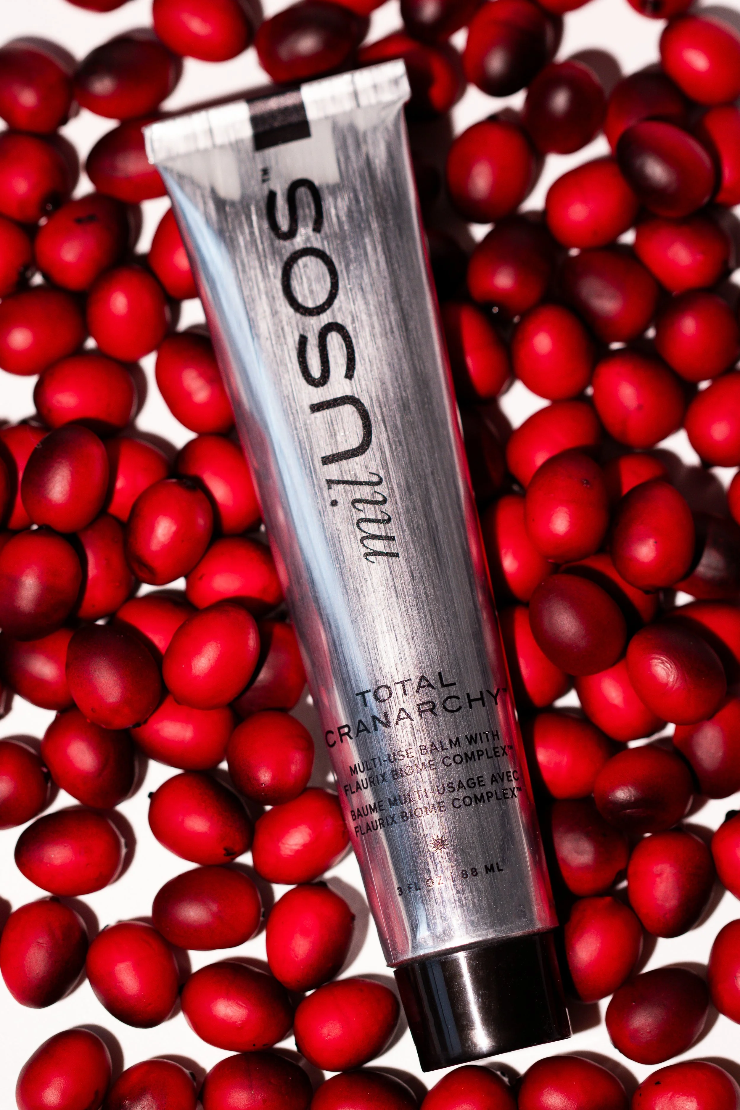A metallic tube of 'U by Moi' Total Cranarchy multi-use balm surrounded by red cranberry berries.