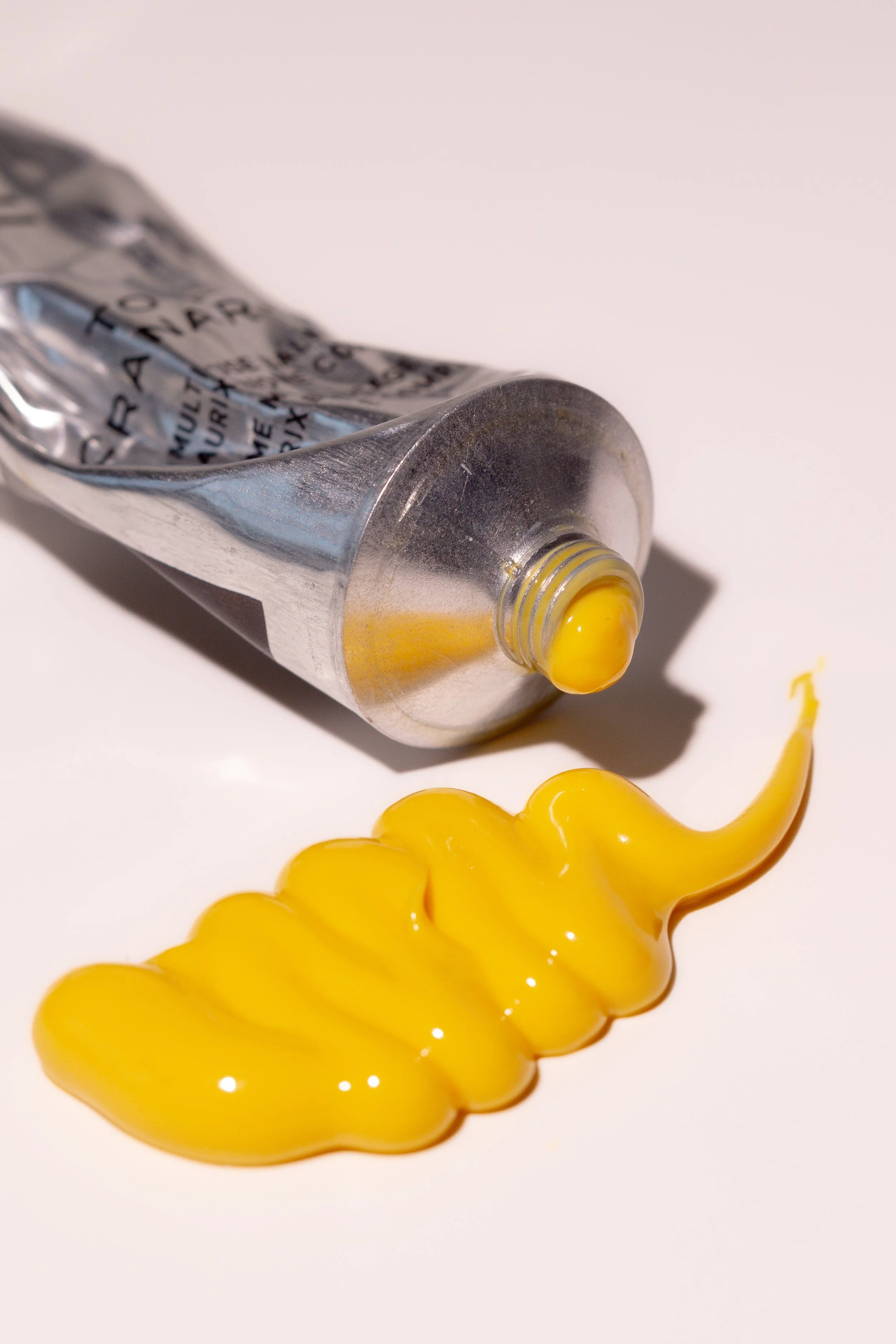 A tube of yellow paint with some paint squeezed out in a spiral on a white surface.