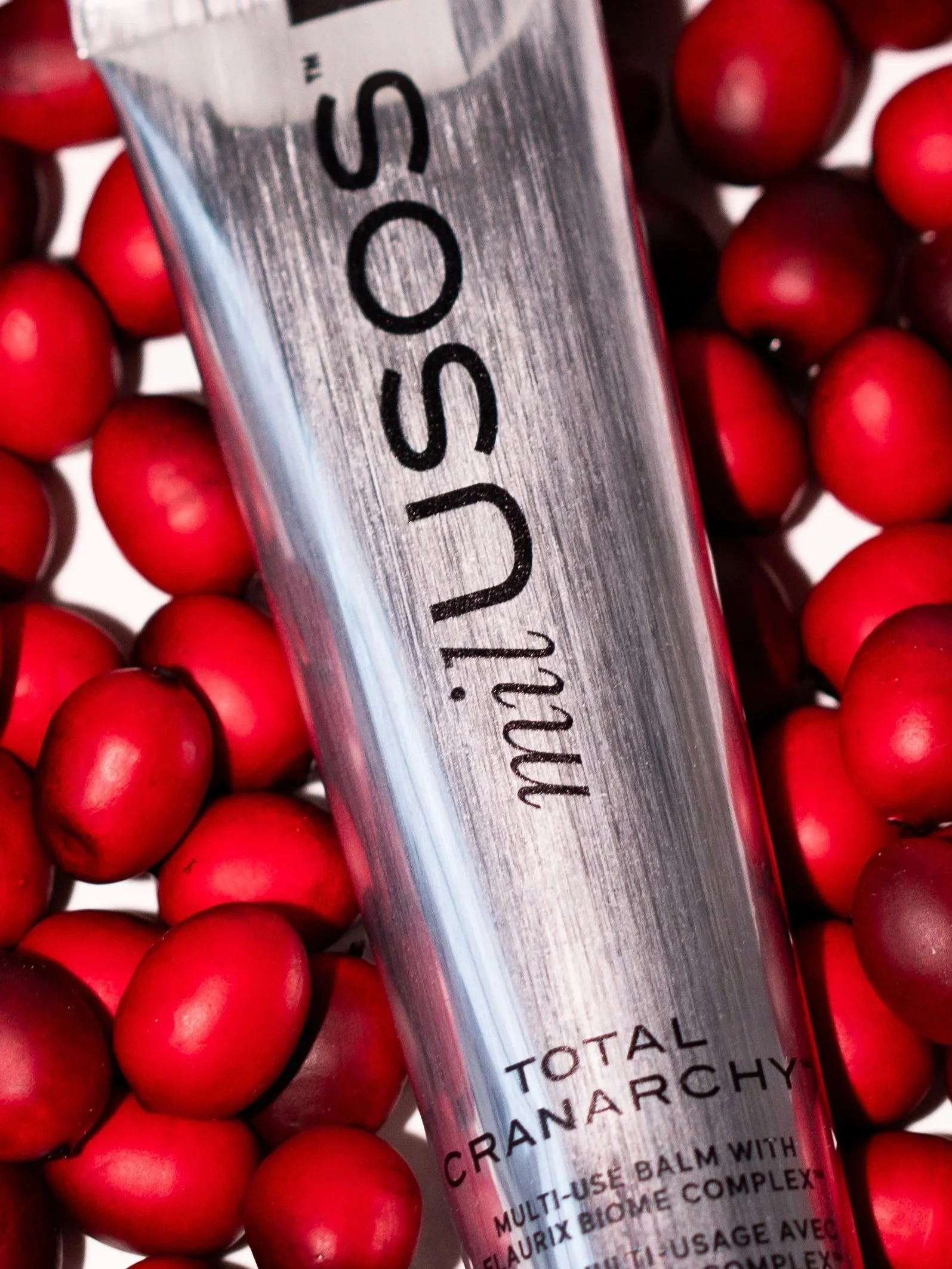 A metallic tube of B.intent Total Cranarchy lip balm surrounded by red cranberries.