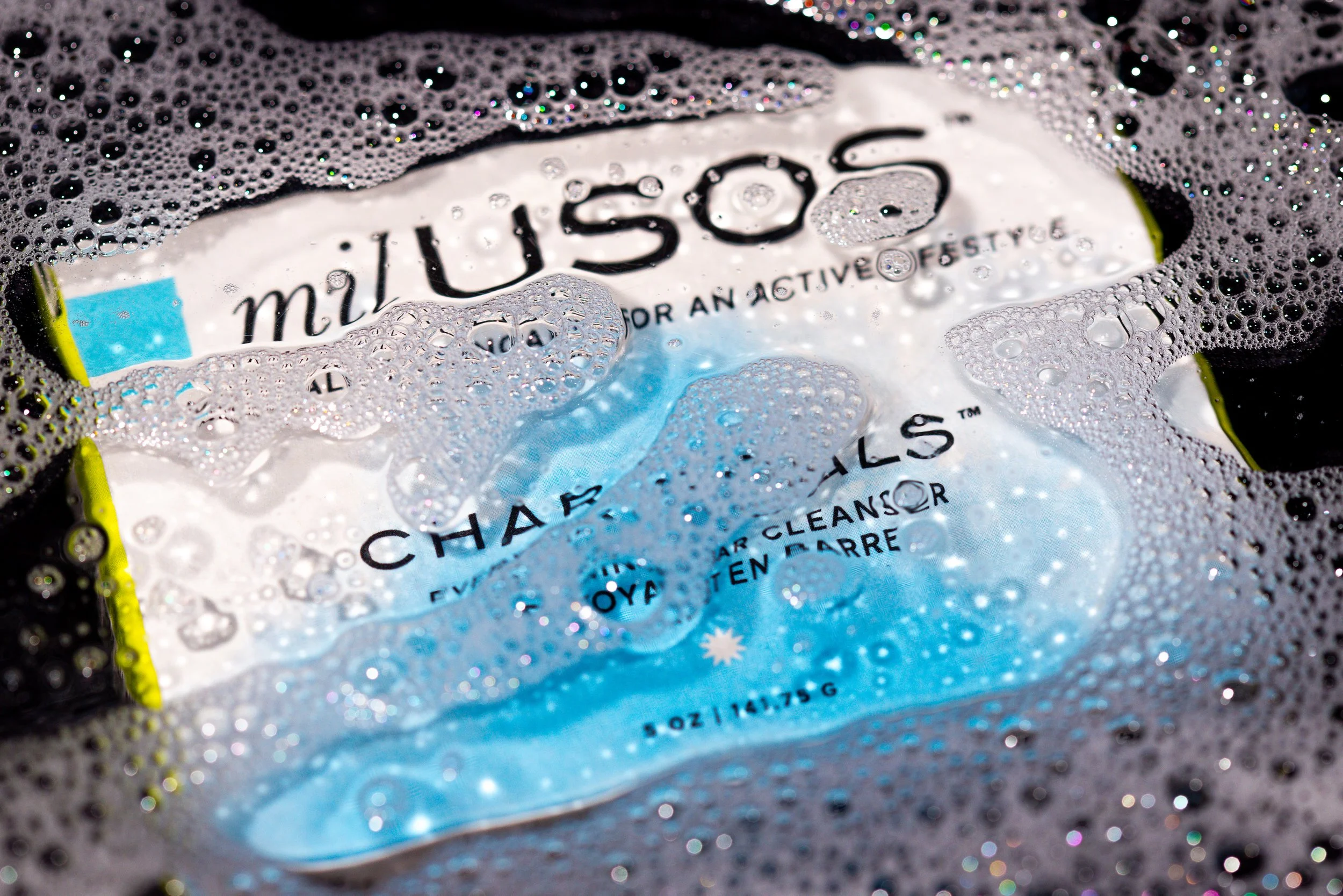 Close-up of a Miu Miu soap bar submerged in soapy water with bubbles, showing the brand name and packaging details.