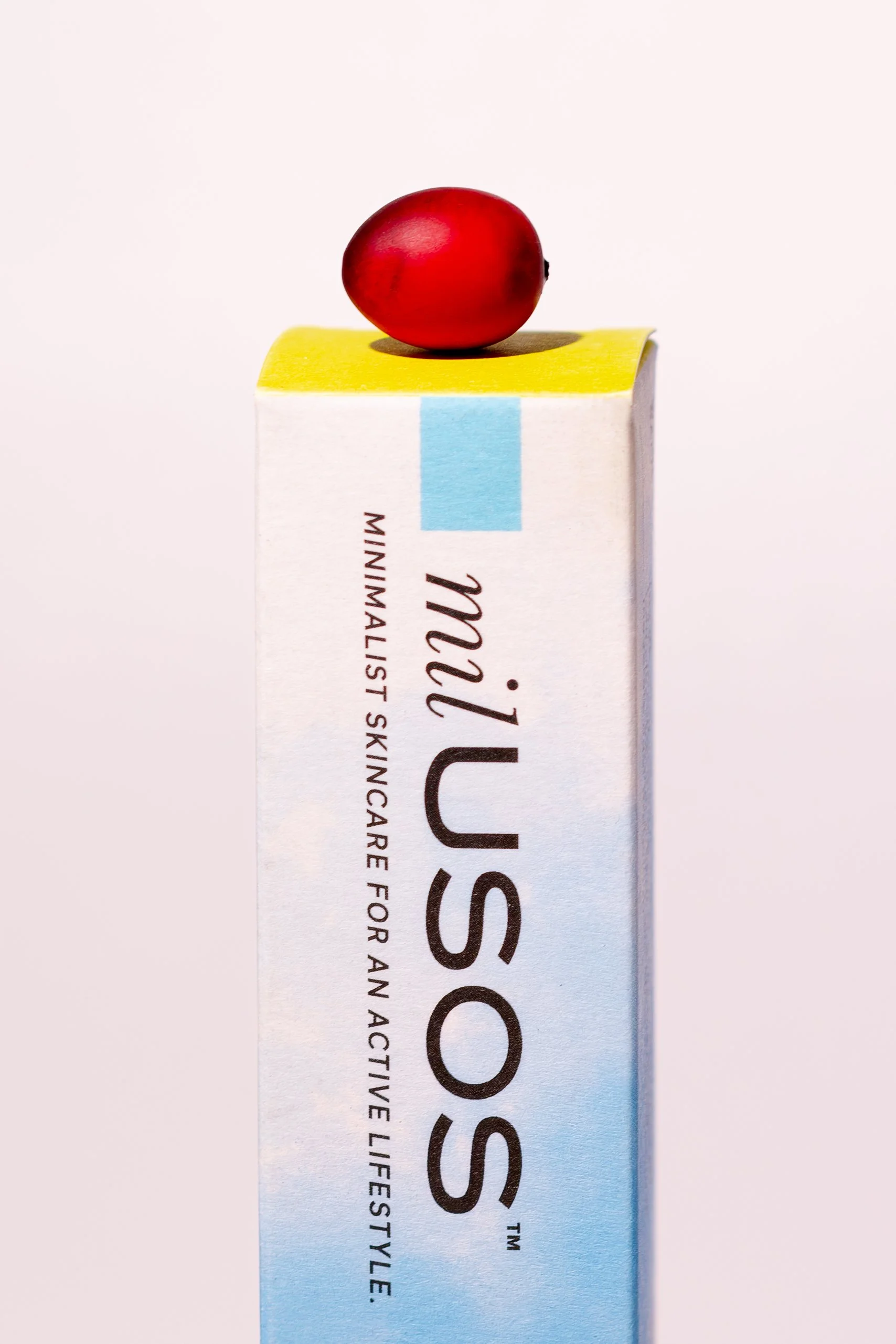 A small red berry placed on top of a carton of Milk US, a skincare product.